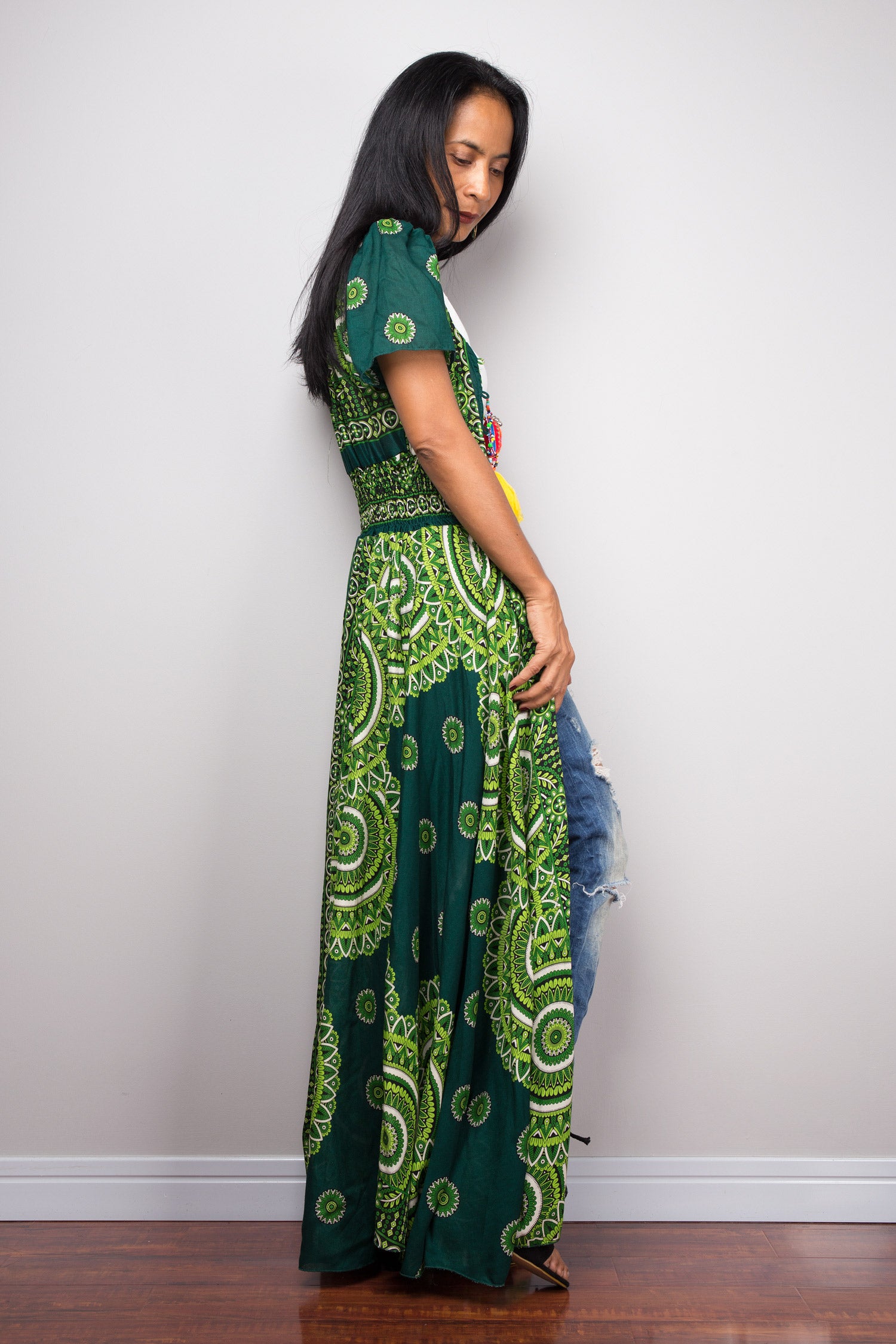 Woman wearing a green and black patterned dress against a white wall.