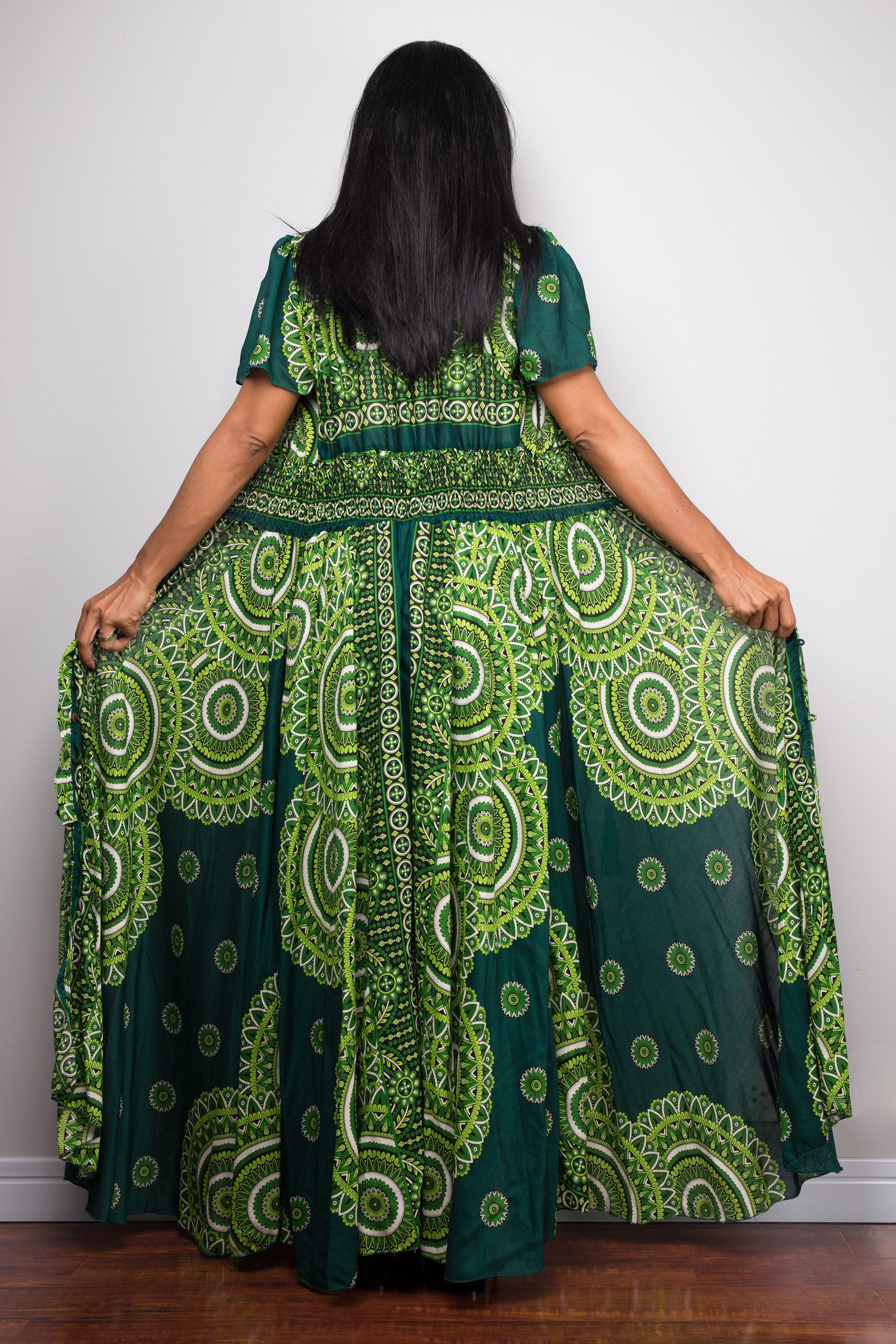 Nuichan wearing a green and white patterned summer maxi dress against a white wall.