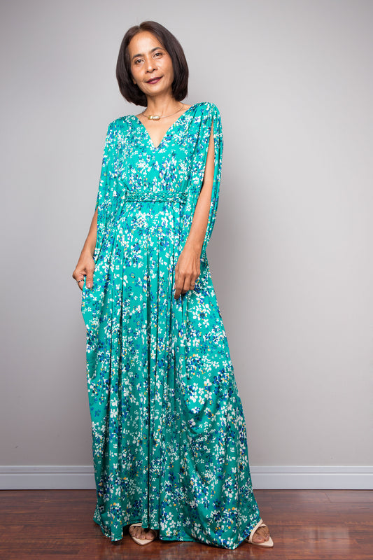 Woman wearing a teal floral caftan dress against a gray background