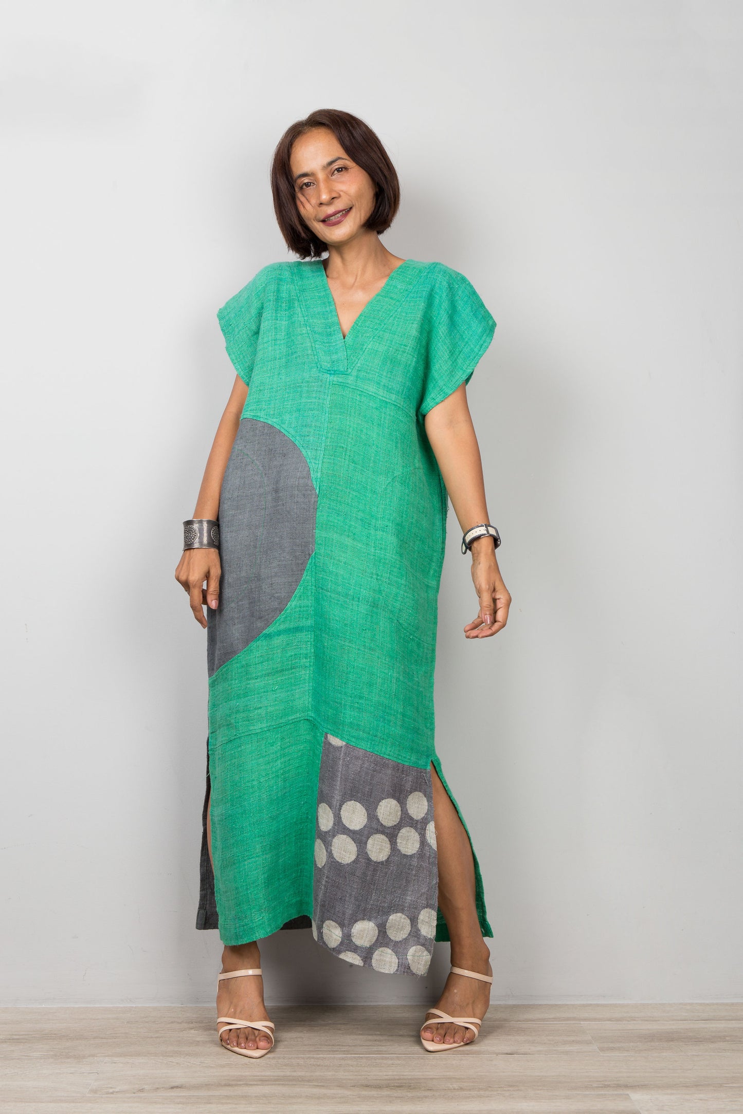 Woman wearing a green and gray dress with a patchwork design on a plain background