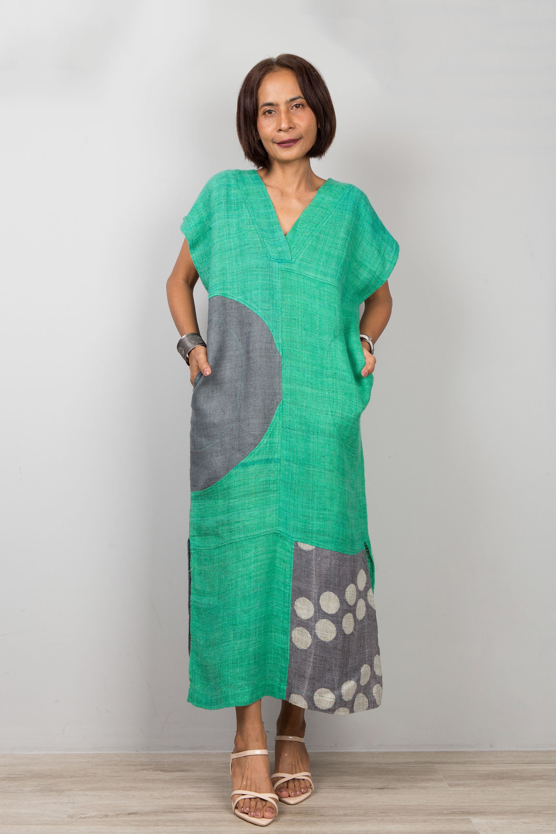 Woman wearing a green dress with gray and white patterned sections on a plain background