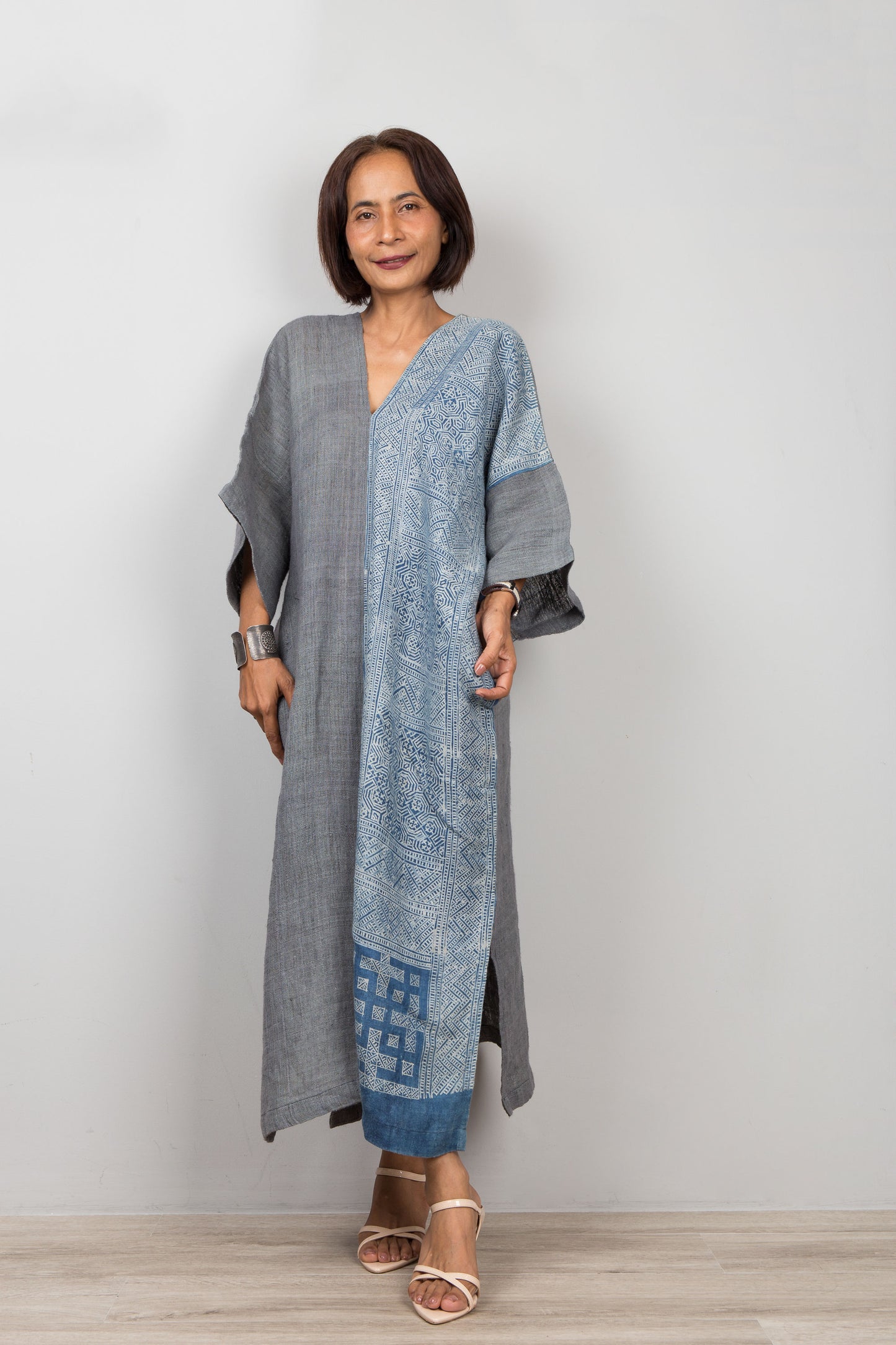 Woman wearing a gray and indigo blue hemp caftan dress with a geometric batik pattern on a plain background