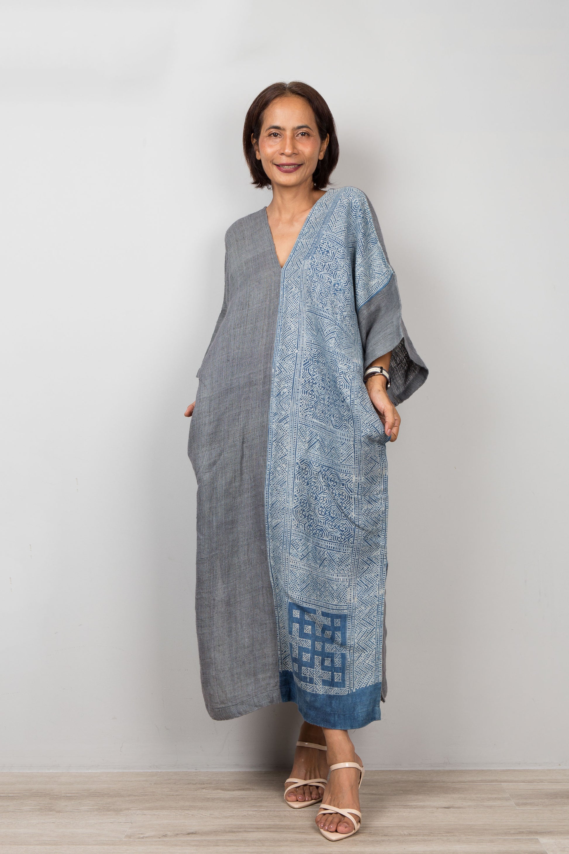 Nuichan wearing a gray and indigo blue hemp caftan dress with a geometric batik tie dye pattern on a plain background