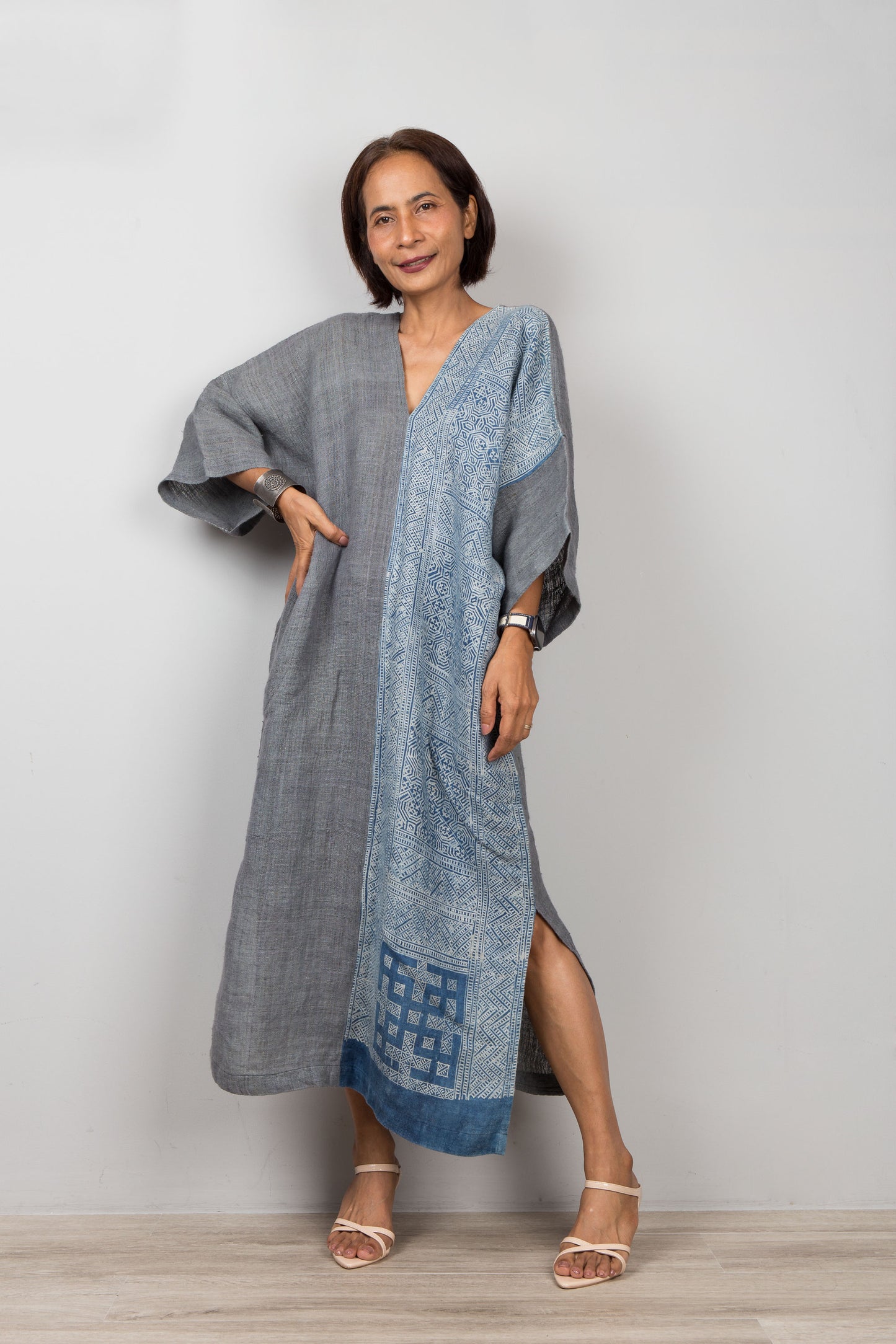 Woman wearing a gray and indigo blue hemp kaftan dress with a geometric batik pattern on a plain background