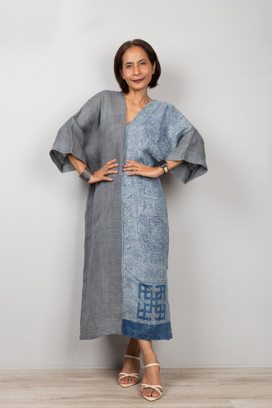 Woman wearing a gray and indigo blue hemp kaftan dress with a geometric pattern on a plain background