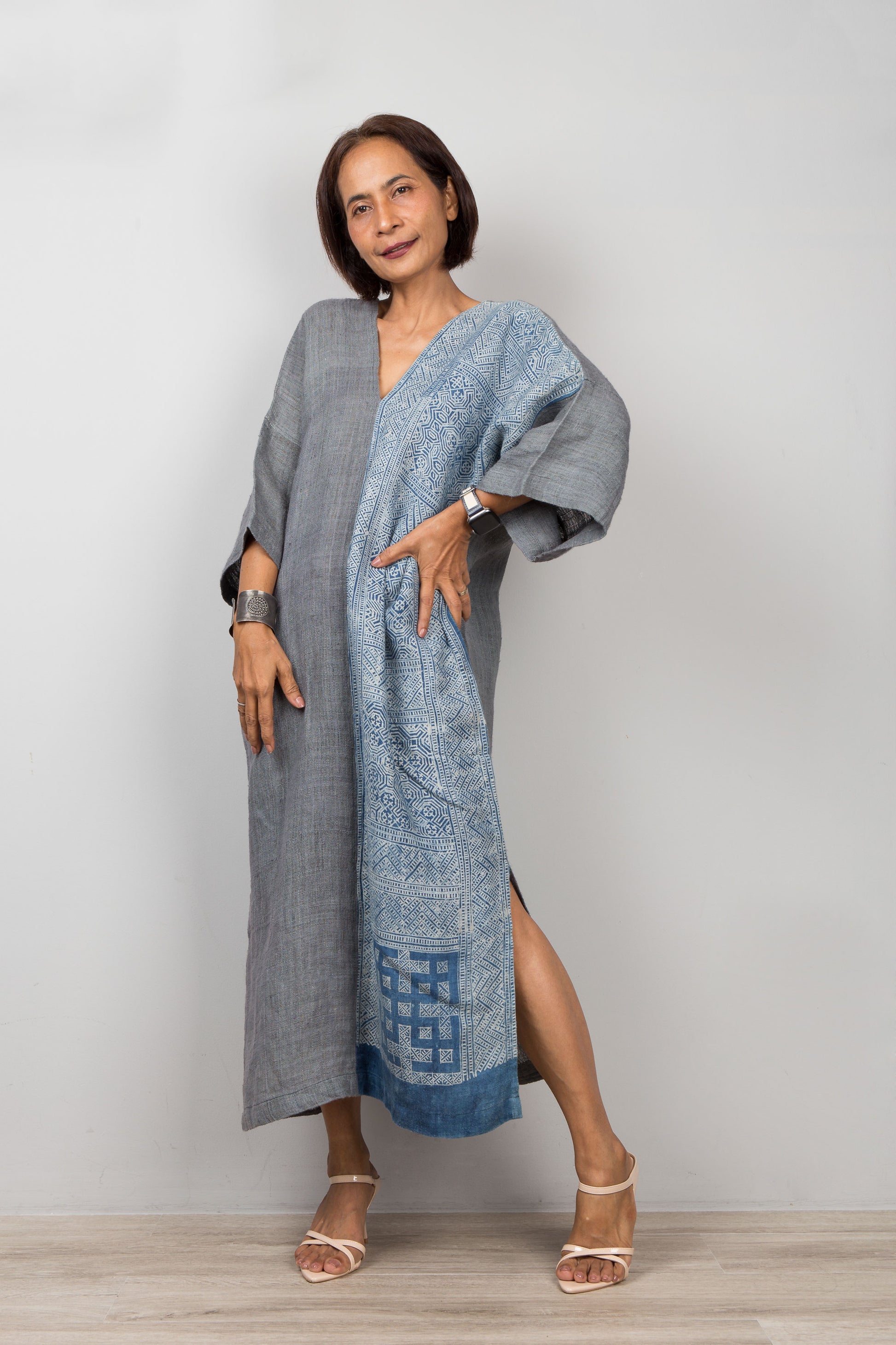 Woman wearing a gray and indigo blue hemp kaftan with a geometric batik tie dye pattern on a plain background