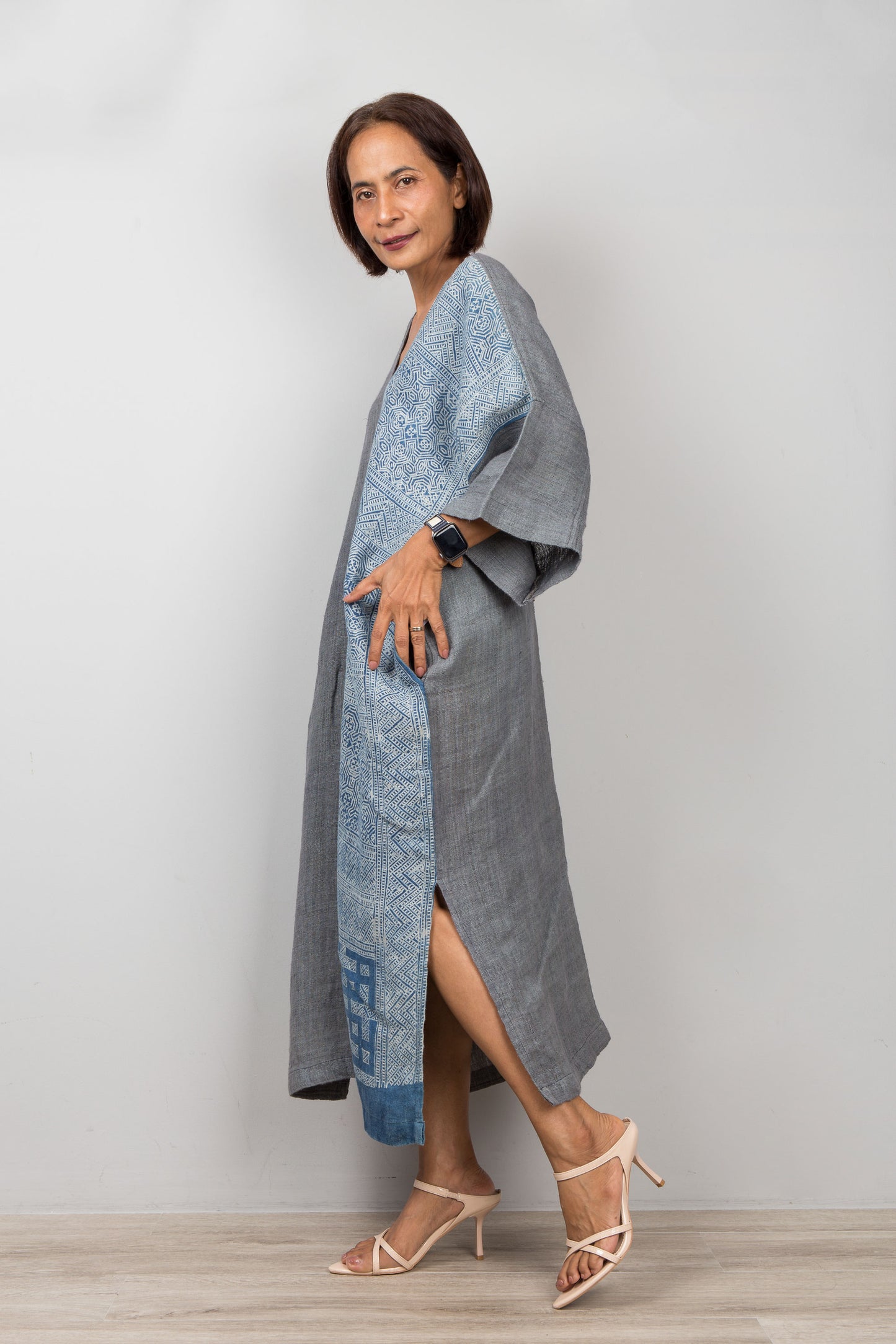 Nuichan wearing a gray and indigo blue hemp kaftan dress with a geometric pattern on a plain background