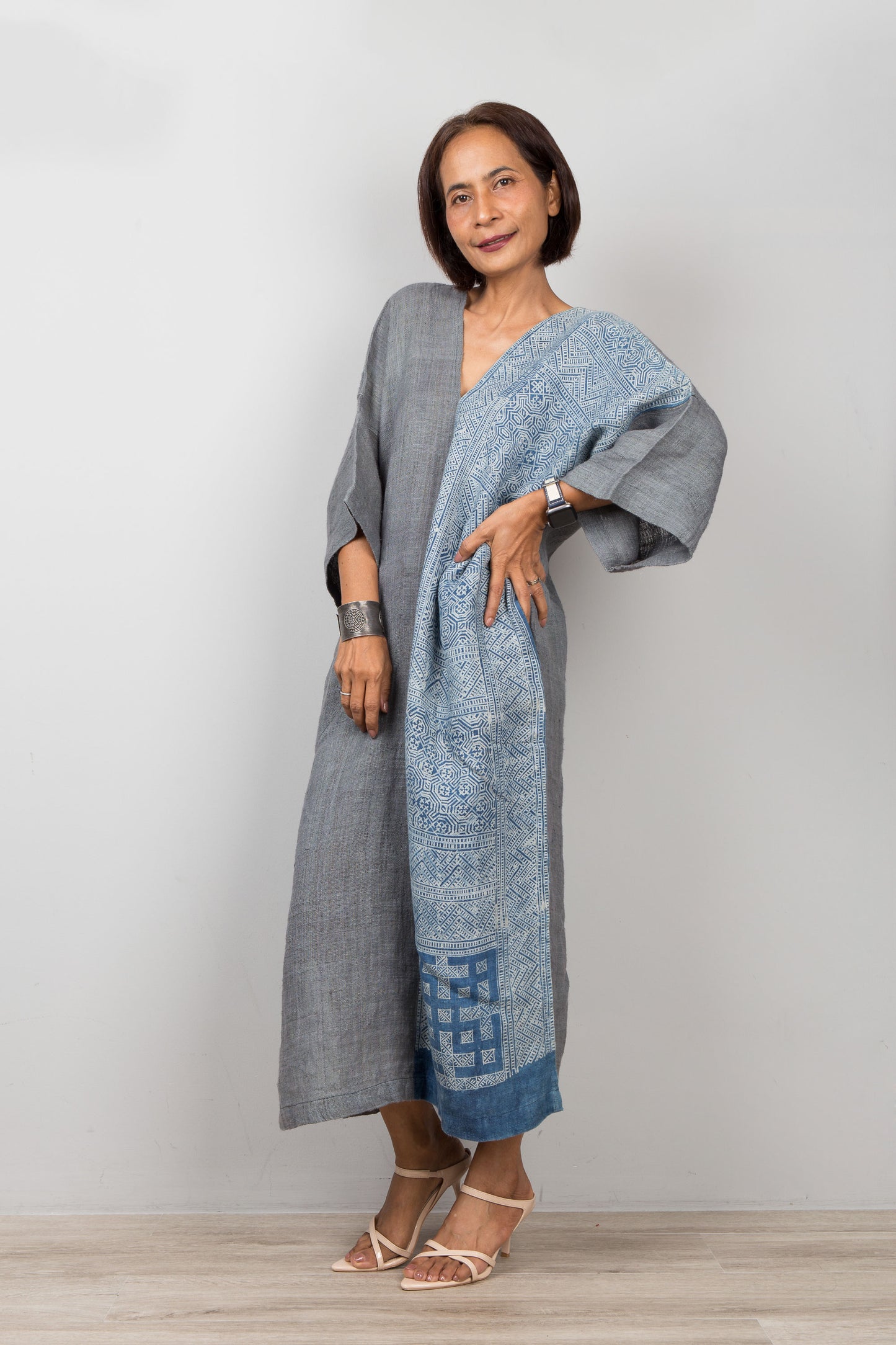 Woman wearing a long, light blue and gray dress with a patterned design against a plain background
