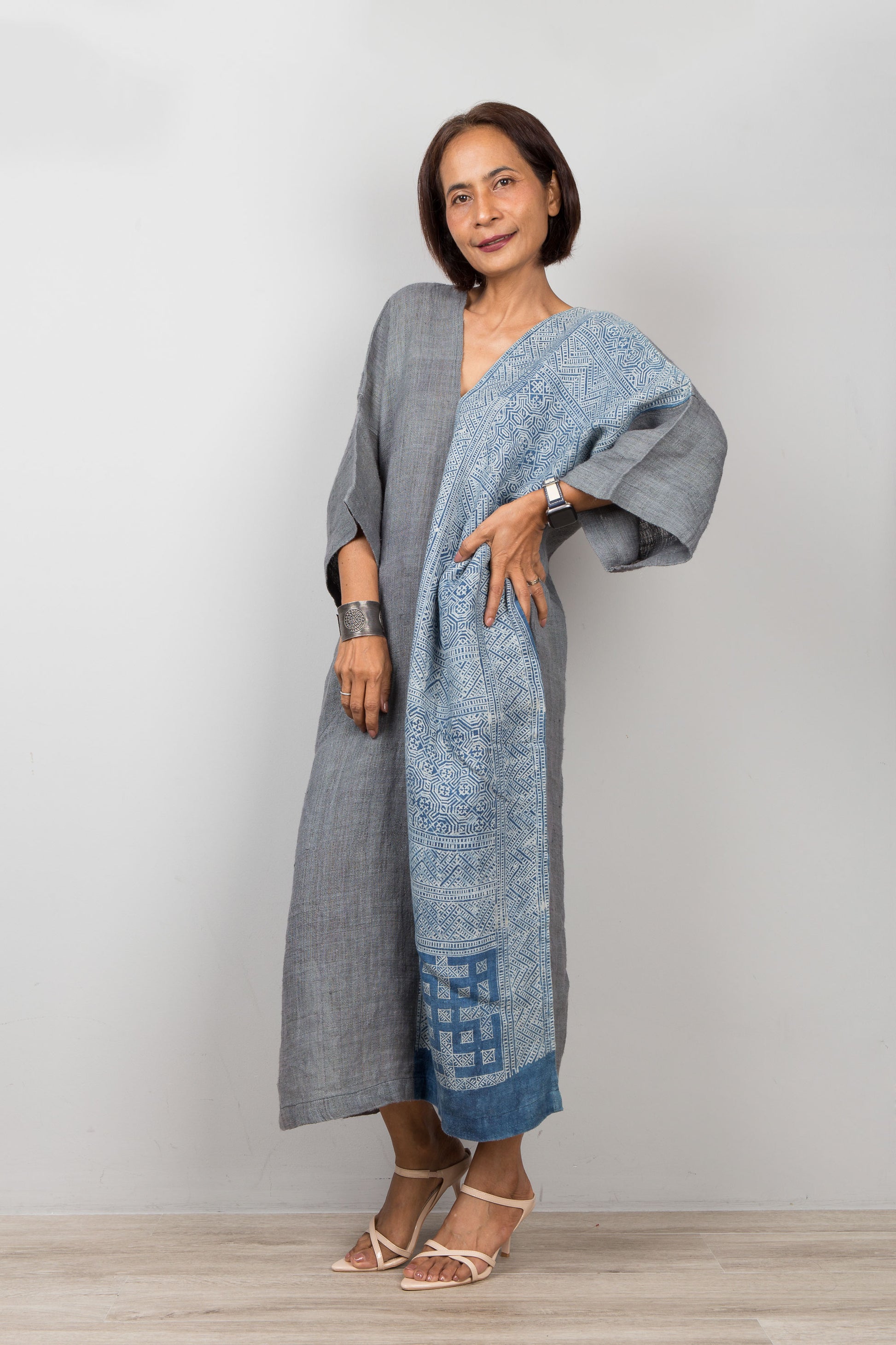 Woman wearing a long, light blue and gray dress with a patterned design against a plain background