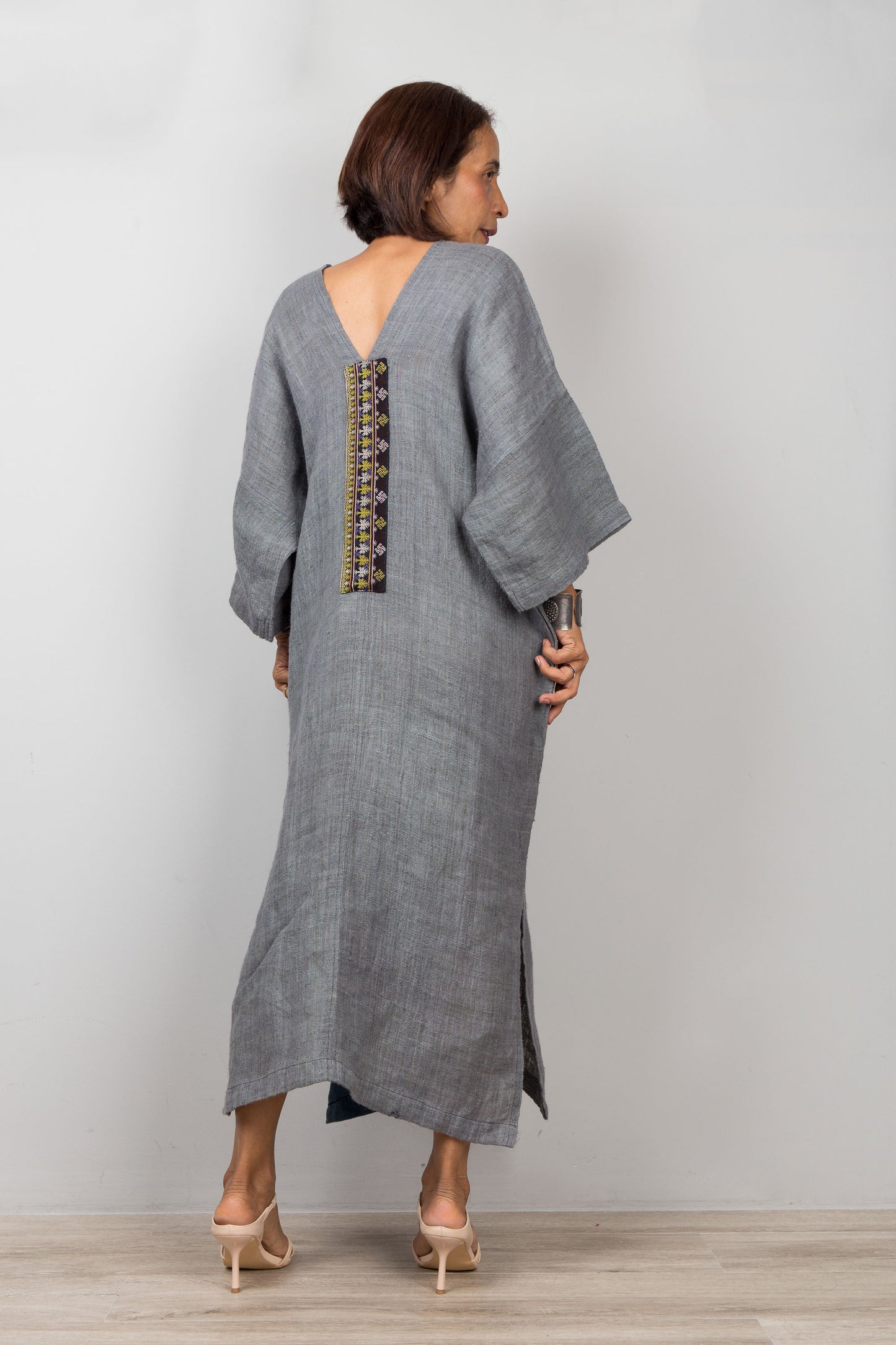 Nuichan wearing a gray and indigo blue hemp caftan dress with a geometric tie dye pattern on a plain background