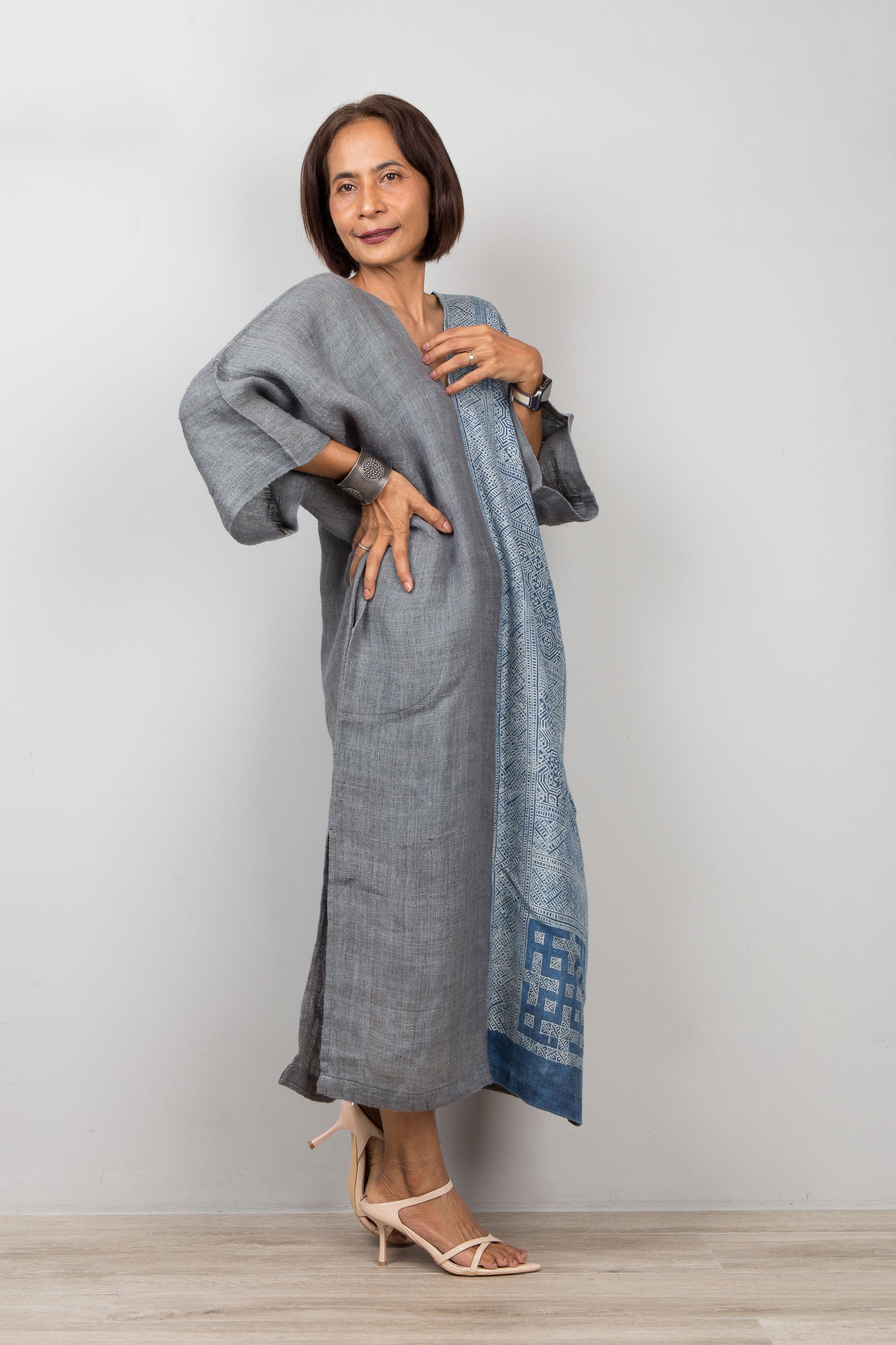 Woman wearing a gray and indigo blue hemp caftan with a geometric pattern on a plain background