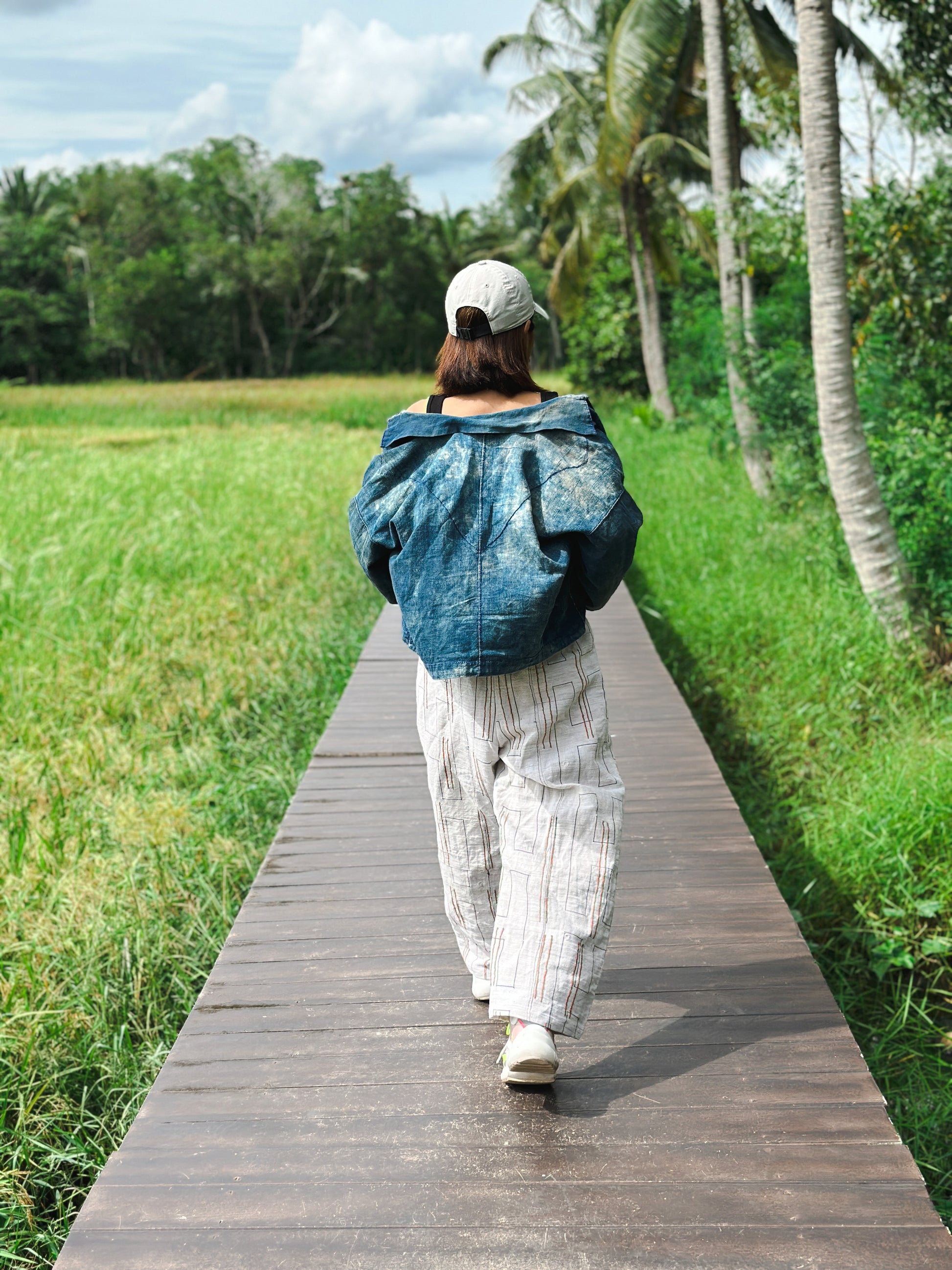 Woman wearing handwoven hemp harem pants with a natural striped pattern, perfect for casual outings or festivals. These boho harem pants, paired with a black crop top and sneakers, are photographed on a wooden boardwalk in a scenic outdoor setting.