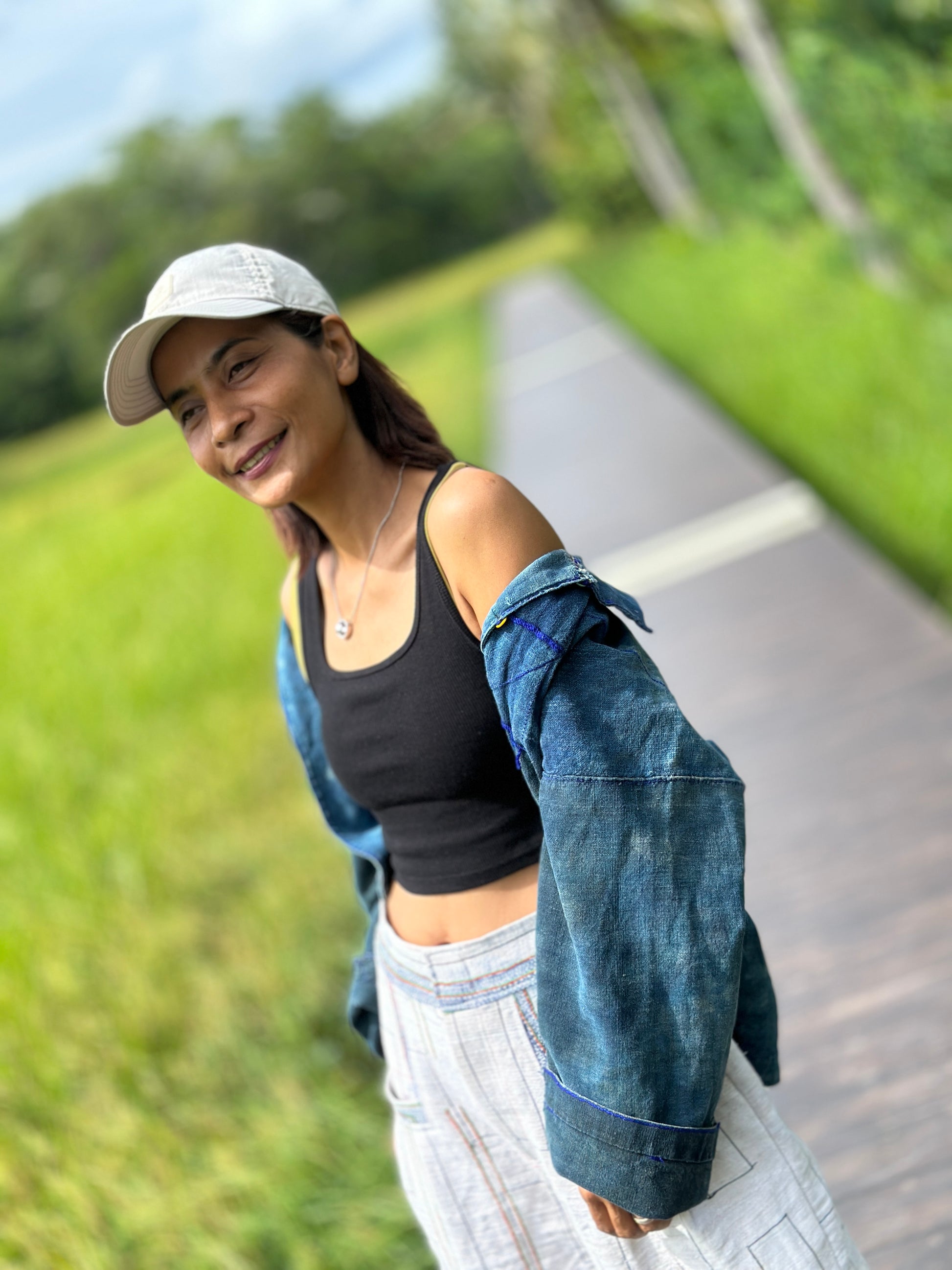 Model in handwoven hemp harem pants with a natural beige tone and striped pattern, standing on a wooden boardwalk surrounded by lush greenery and palm trees. These boho harem pants, paired with a black crop top, exude a free-spirited, nature-inspired vibe.