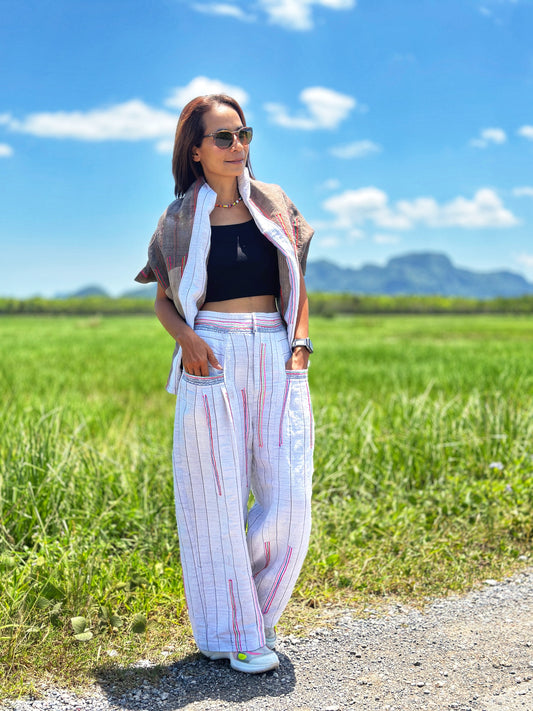 A person standing on a road with a field in the background, wearing handwoven hemp pants with a striped pattern and a top, sunglasses, and sandals.