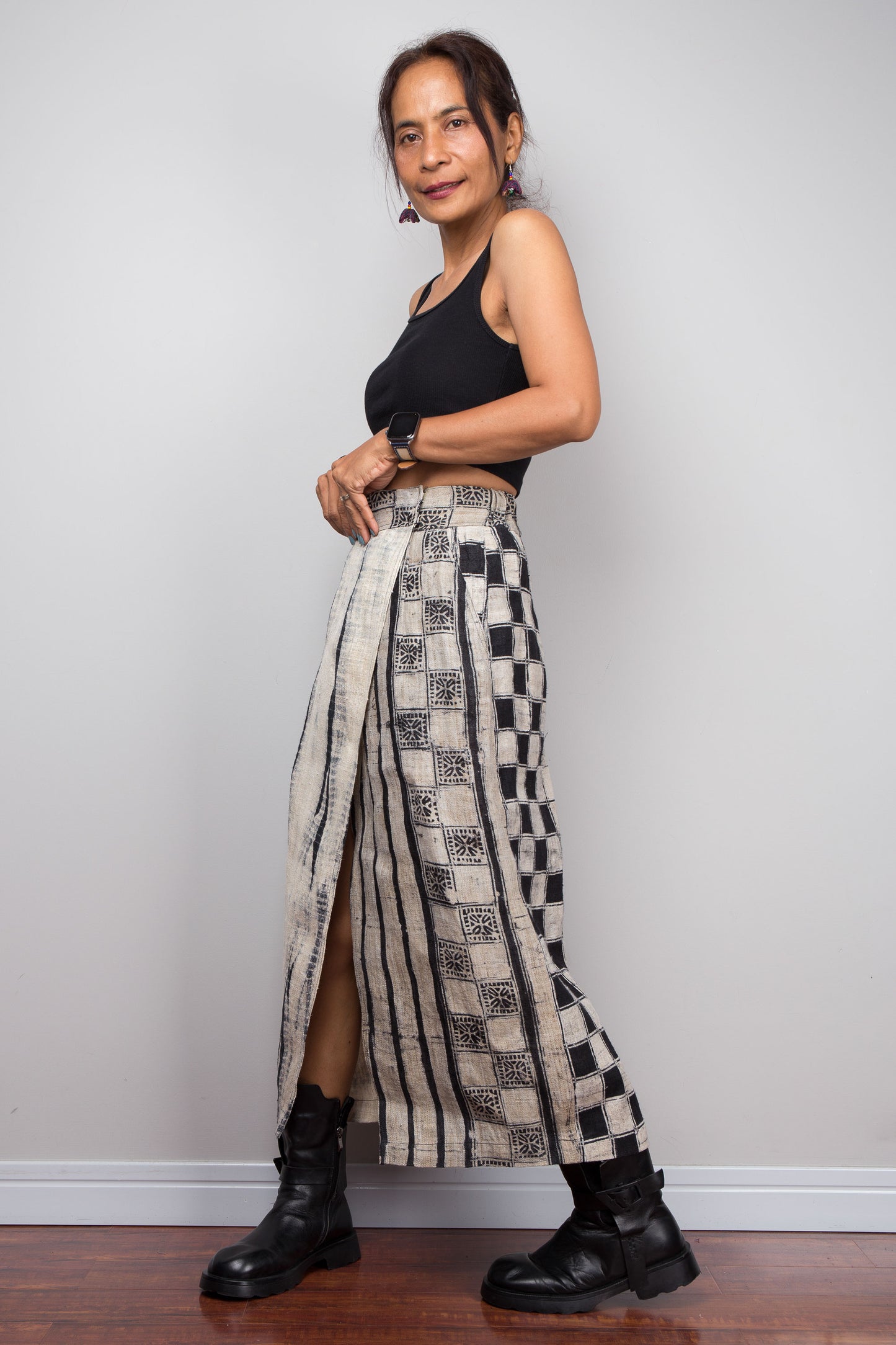 Three-quarter front view of a model wearing the Nuichan handwoven hemp artisan wrap skirt with  front split open, showcasing contrast between the shibori front panel and hand-drawn candle batik checkerboard side panel, and hand-drawn batik geometric waistband in natural ecru and deep black handwoven hemp