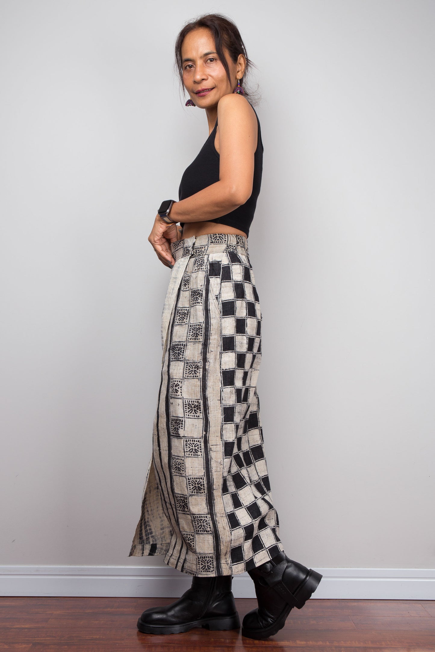 Side view of a model wearing the Nuichan handwoven hemp wrap skirt  displaying the wrap front construction with flat metal hook and bar closures, Japanese shibori vertical lightning stripe pattern on the front panel, hand-drawn batik checkerboard side panel, front split opening, and hand-drawn batik geometric waistband