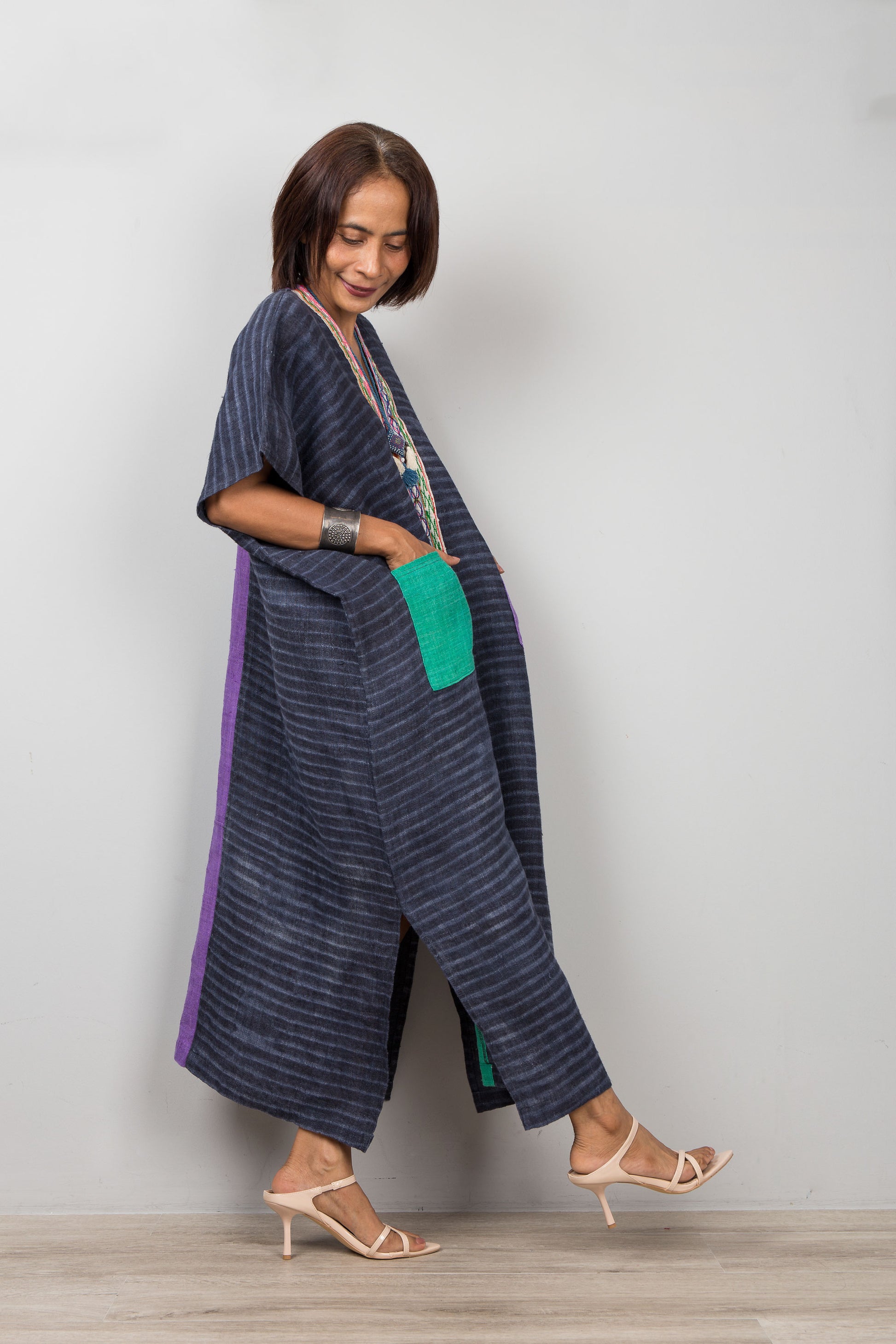 Woman wearing a long dark blue striped hemp dress with green accents on a plain background