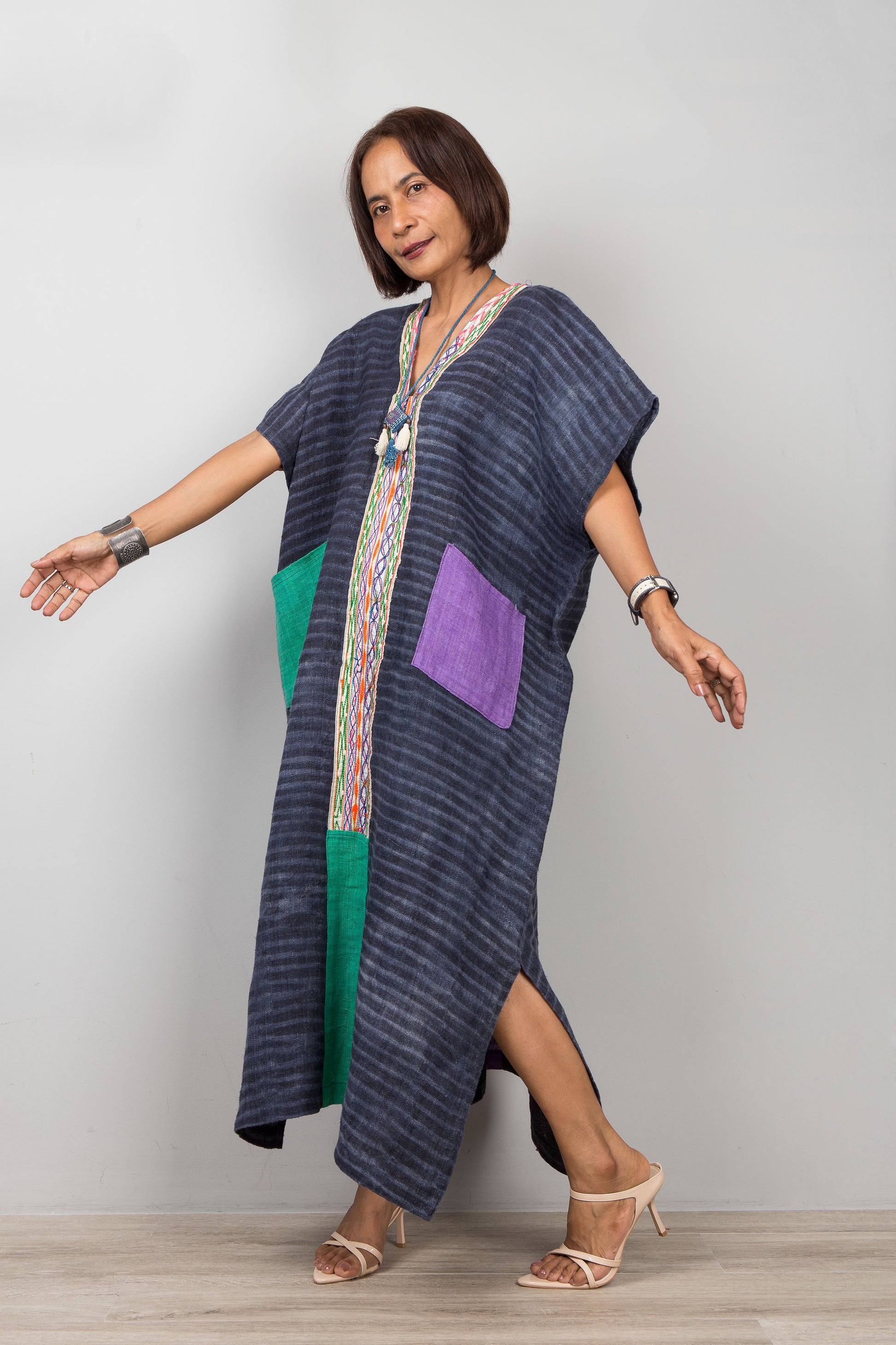Woman wearing a long, dark blue dress with colorful patchwork pockets on a plain background