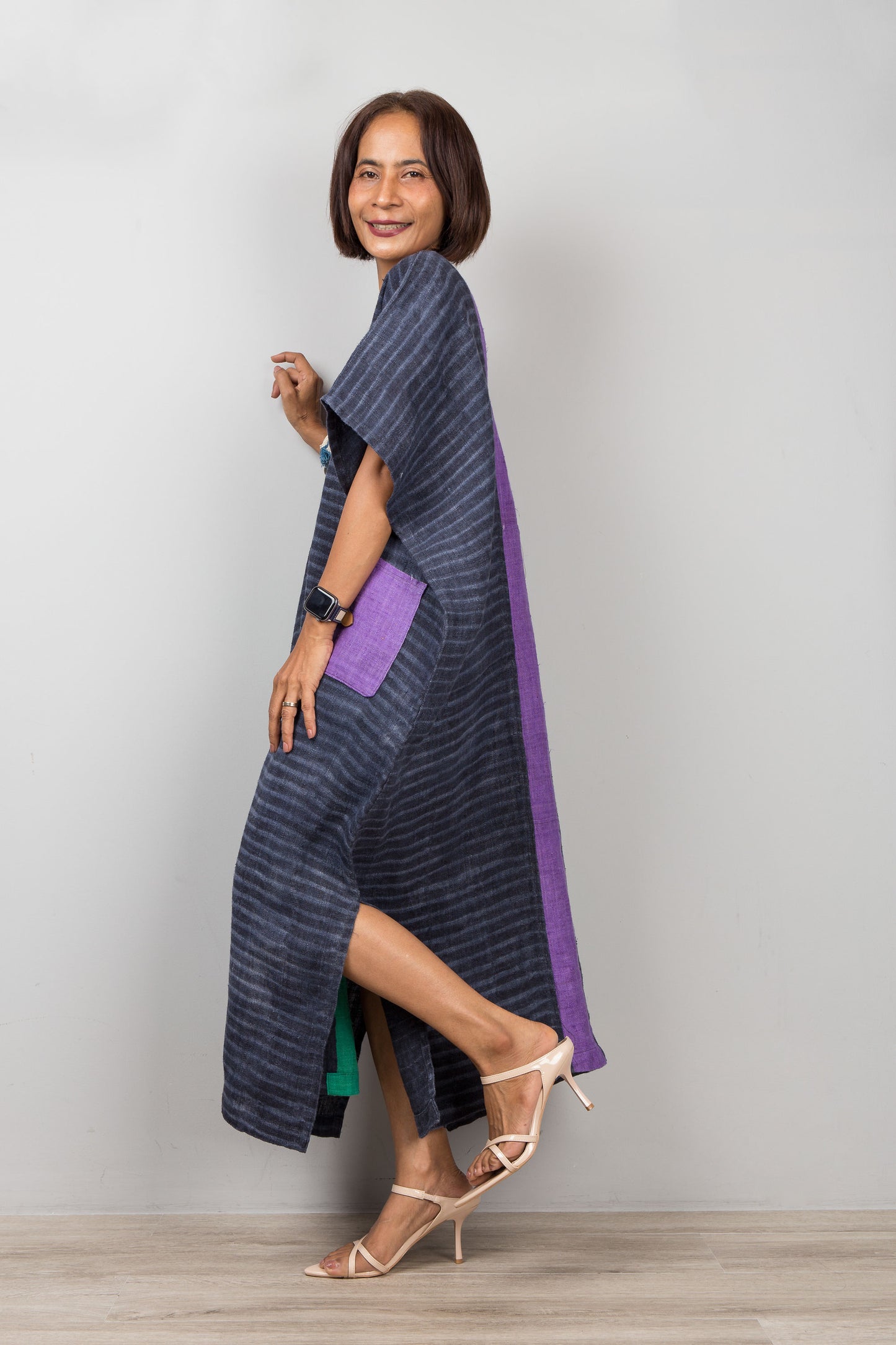 Woman wearing a long, dark blue and purple dress with a slit on a plain background
