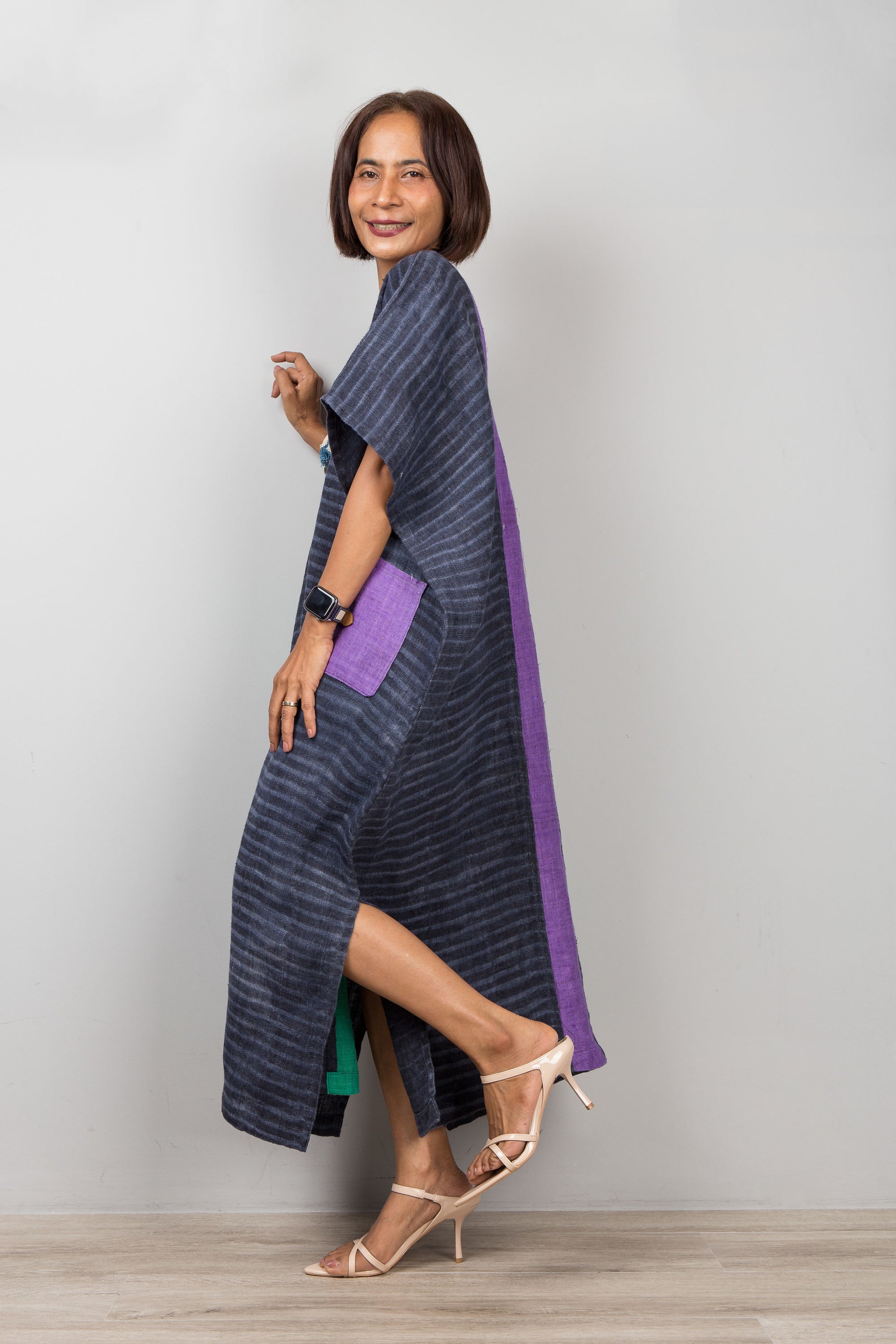 Woman wearing a long, dark blue and purple dress with a slit on a plain background