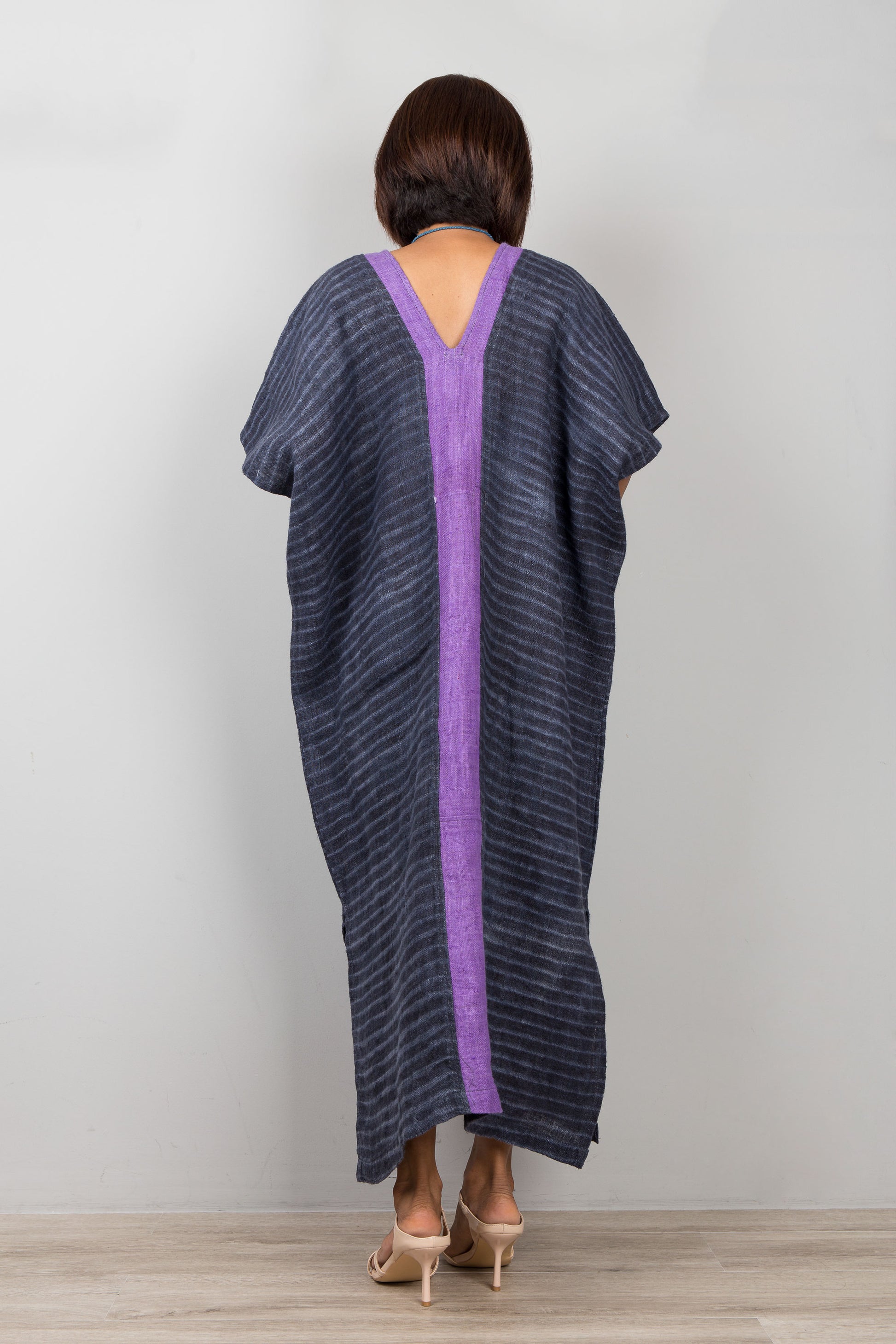 Woman wearing a dark blue hemp kaftan dress with a purple back panel against a plain background