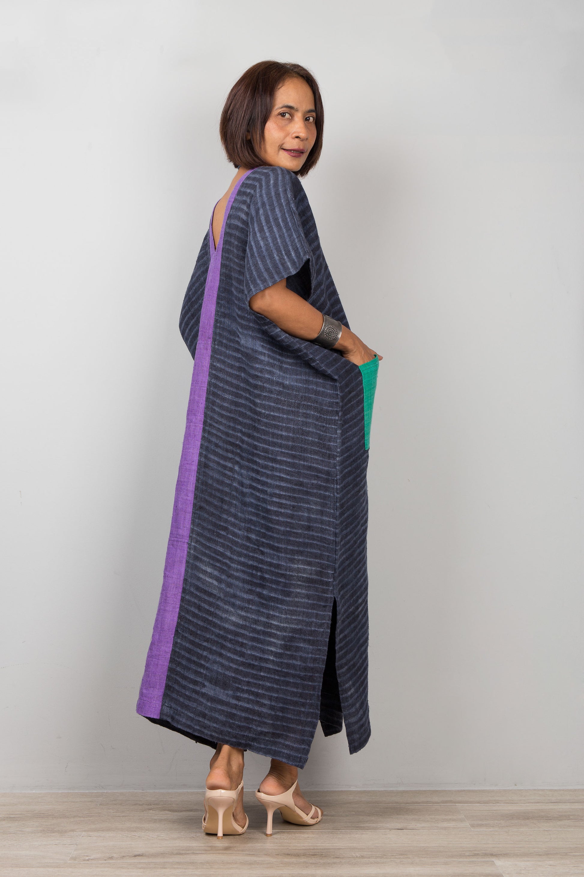 Woman wearing a long, dark blue dress with a purple stripe on a plain background