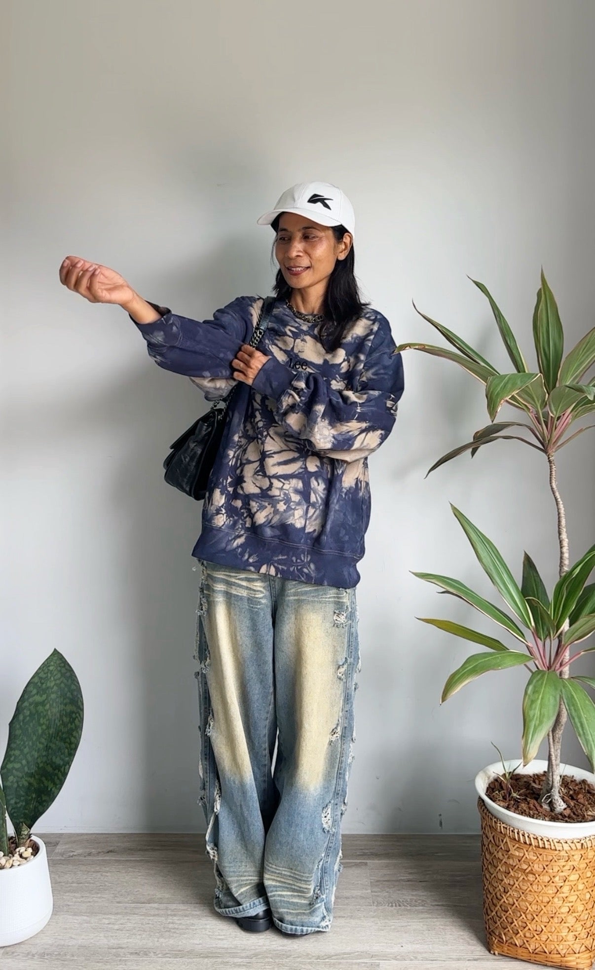 Person wearing a blue patterned sweater and jeans standing indoors with plants around