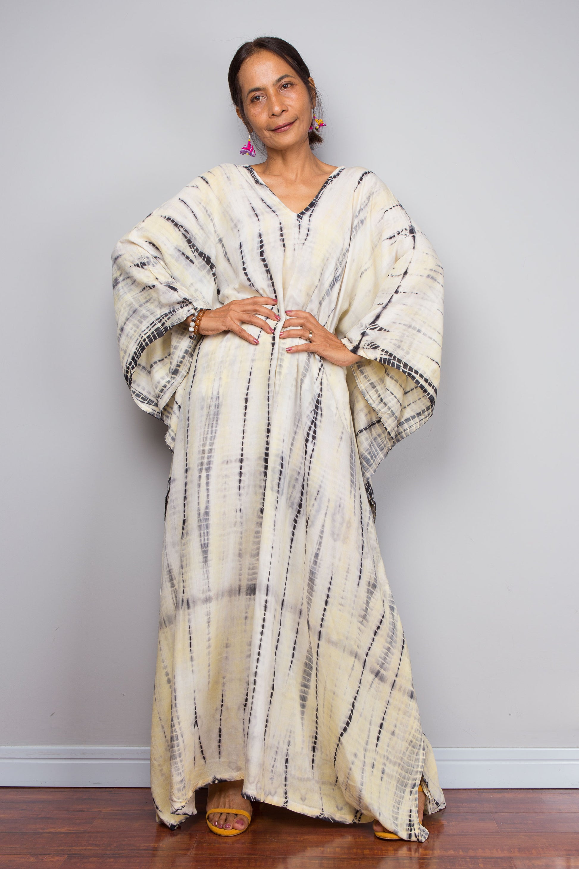 Woman wearing a long, patterned tie dye kaftan dress against a plain background