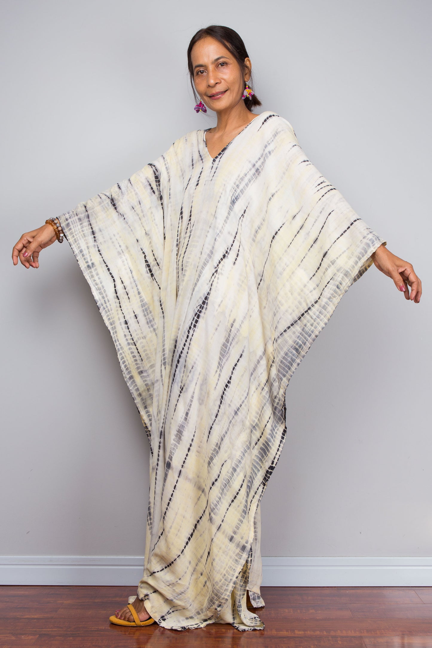 Woman wearing a white, yellow and black patterned caftan against a plain background