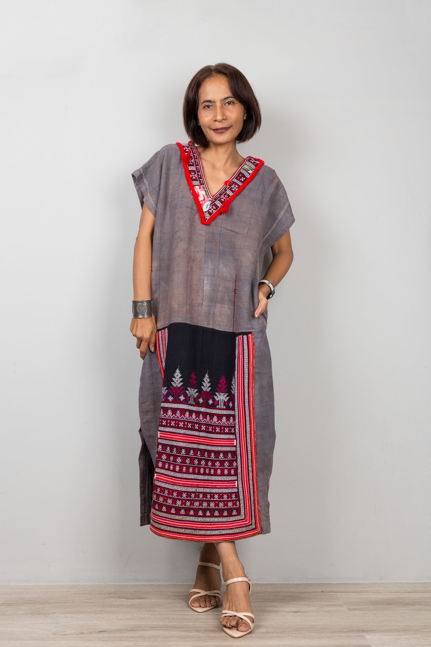 Woman wearing grey , short sleeve, dress with traditional embroidery on the bottom part of the caftan