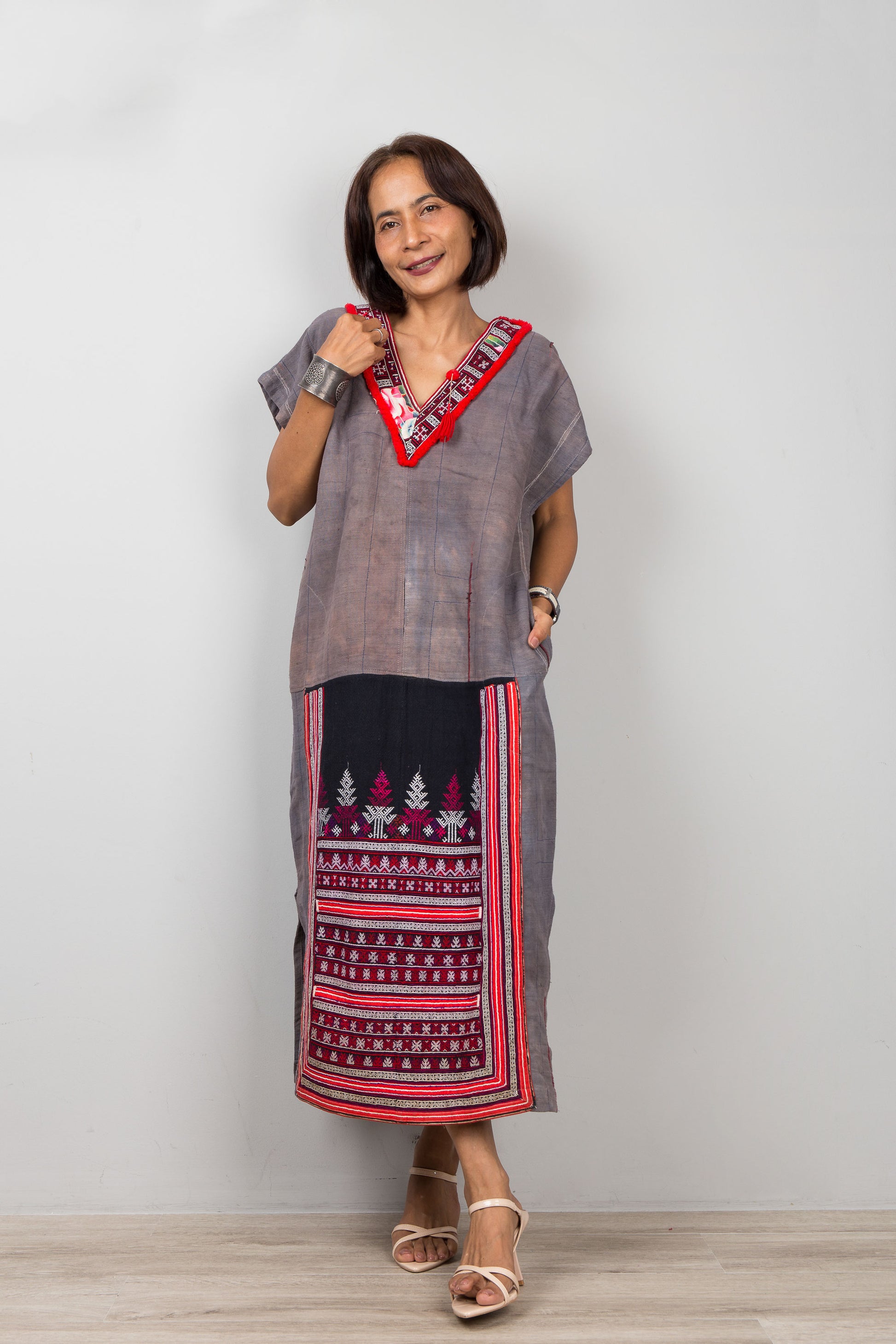 Woman wearing grey , short sleeve, kaftan  with side splits and with traditional embroidery on the bottom part of the caftan
