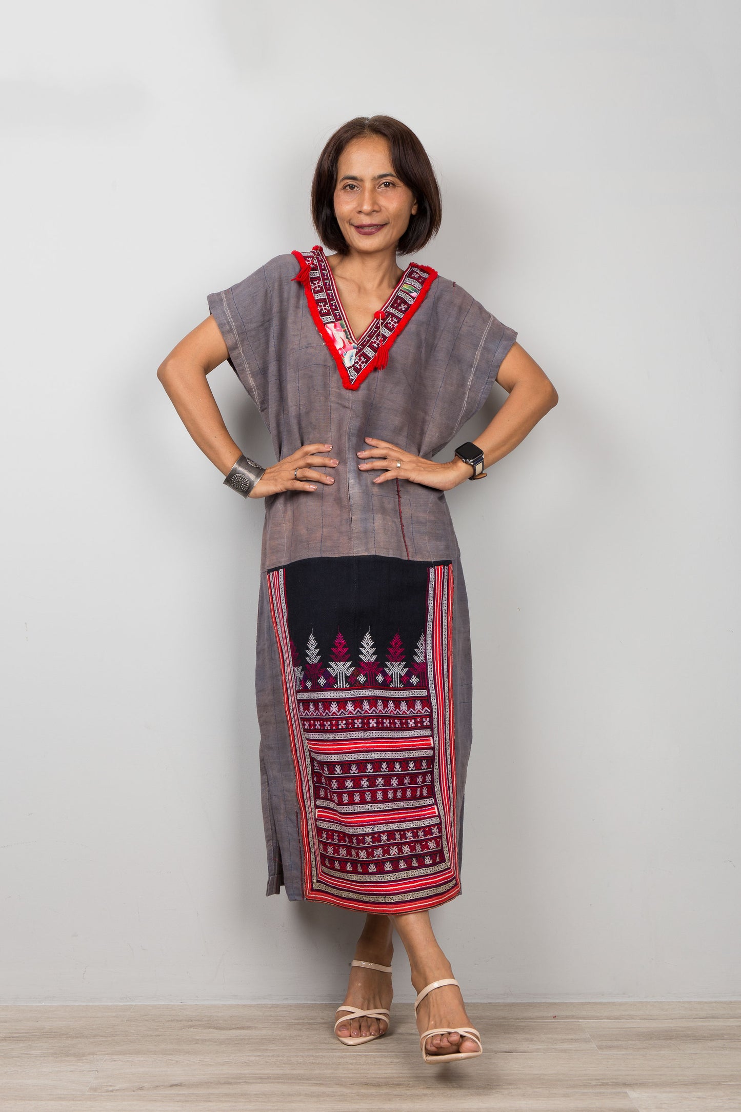 Woman wearing grey , short sleeve, kaftan with traditional embroidery on the bottom part of the dress