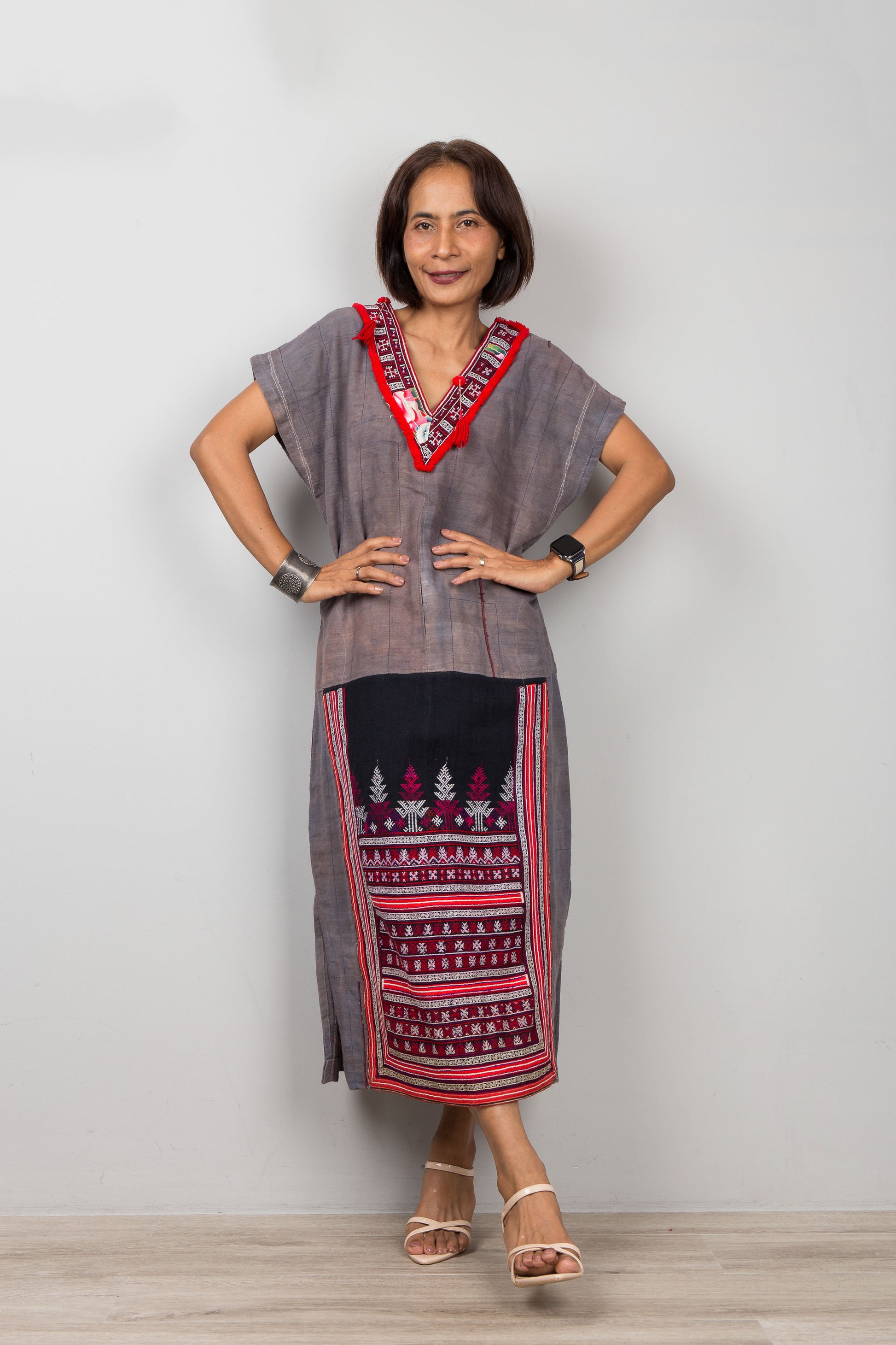 Woman wearing grey , short sleeve, kaftan with traditional embroidery on the bottom part of the dress