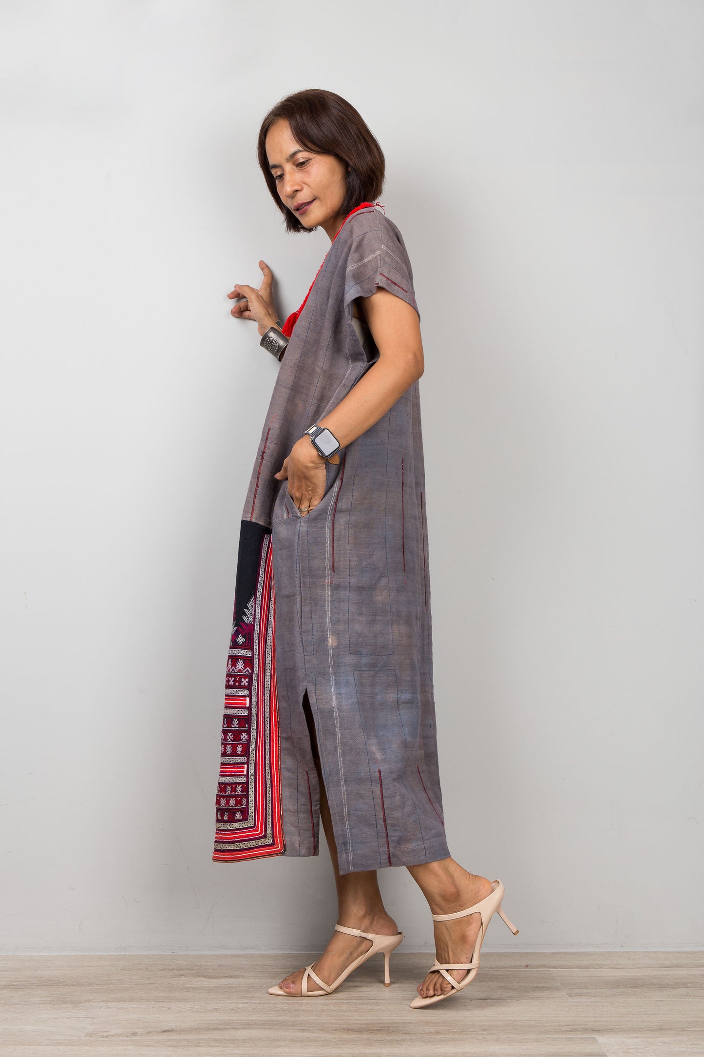Woman wearing grey , short sleeve, kaftan  with side splits and with traditional embroidery on the bottom part of the dress