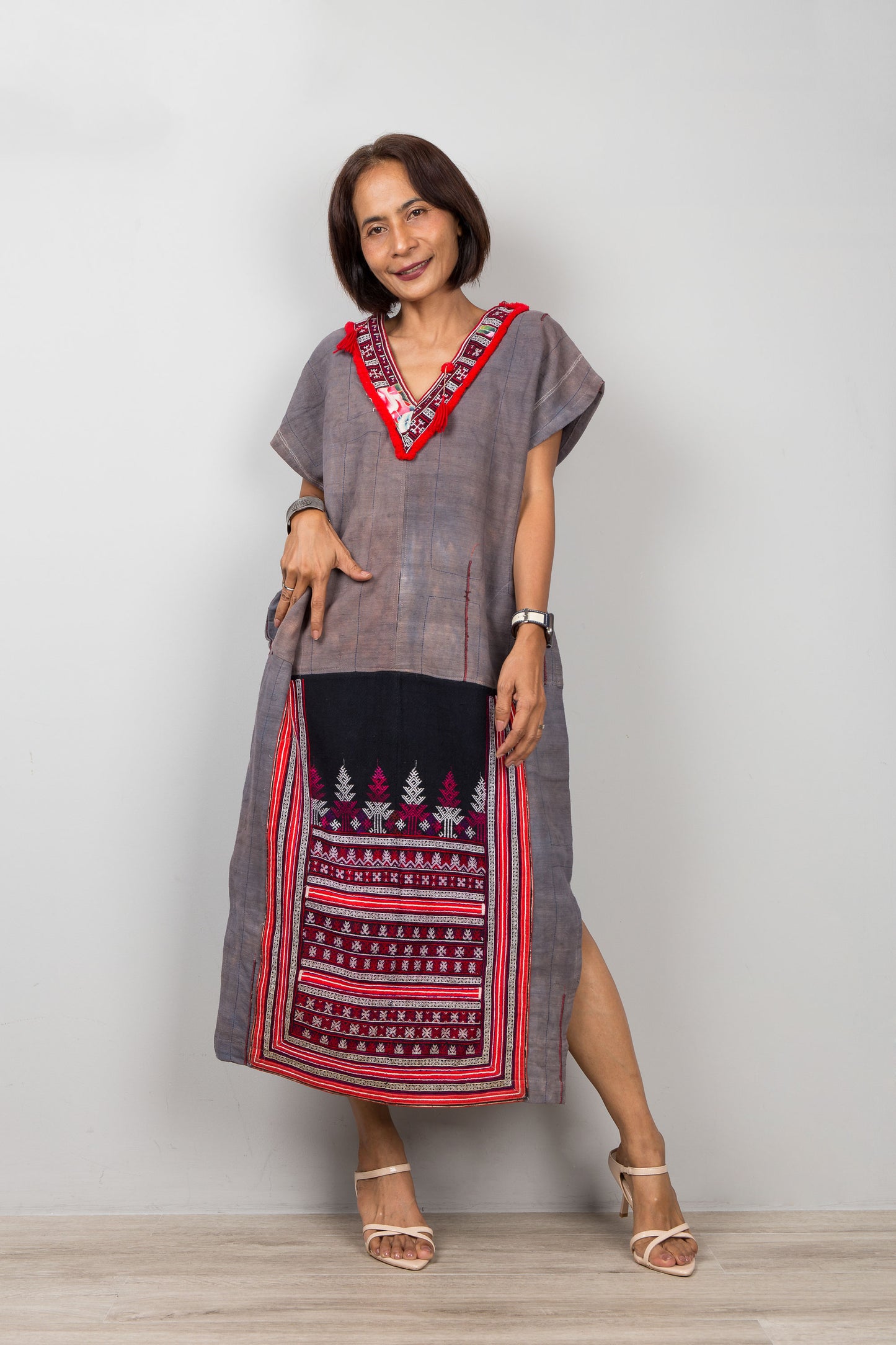 Woman wearing a long, grey dress with embroidered bottom part on a plain background