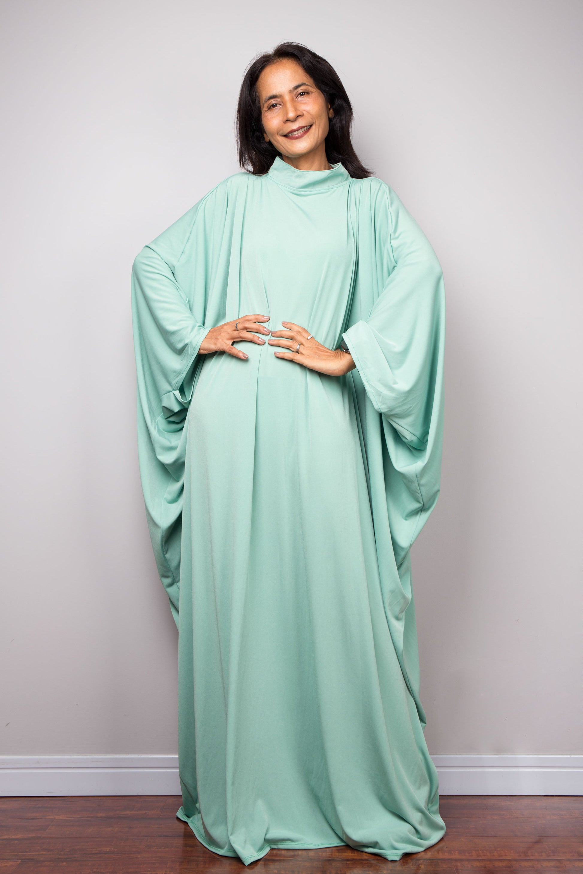 Woman wearing a mint green caftan maxi dress against a plain background
