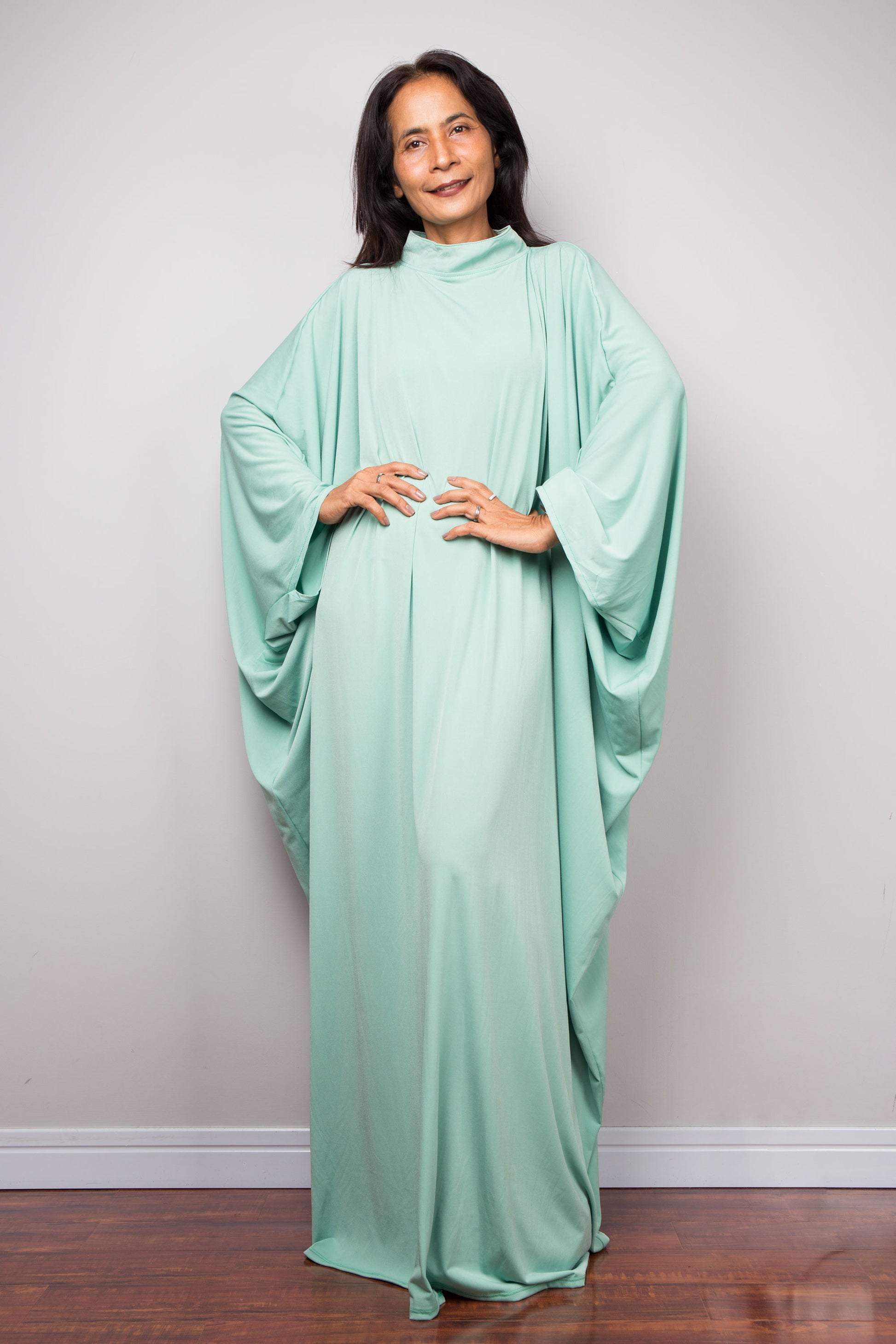 Woman wearing a mint green caftan dress against a plain background
