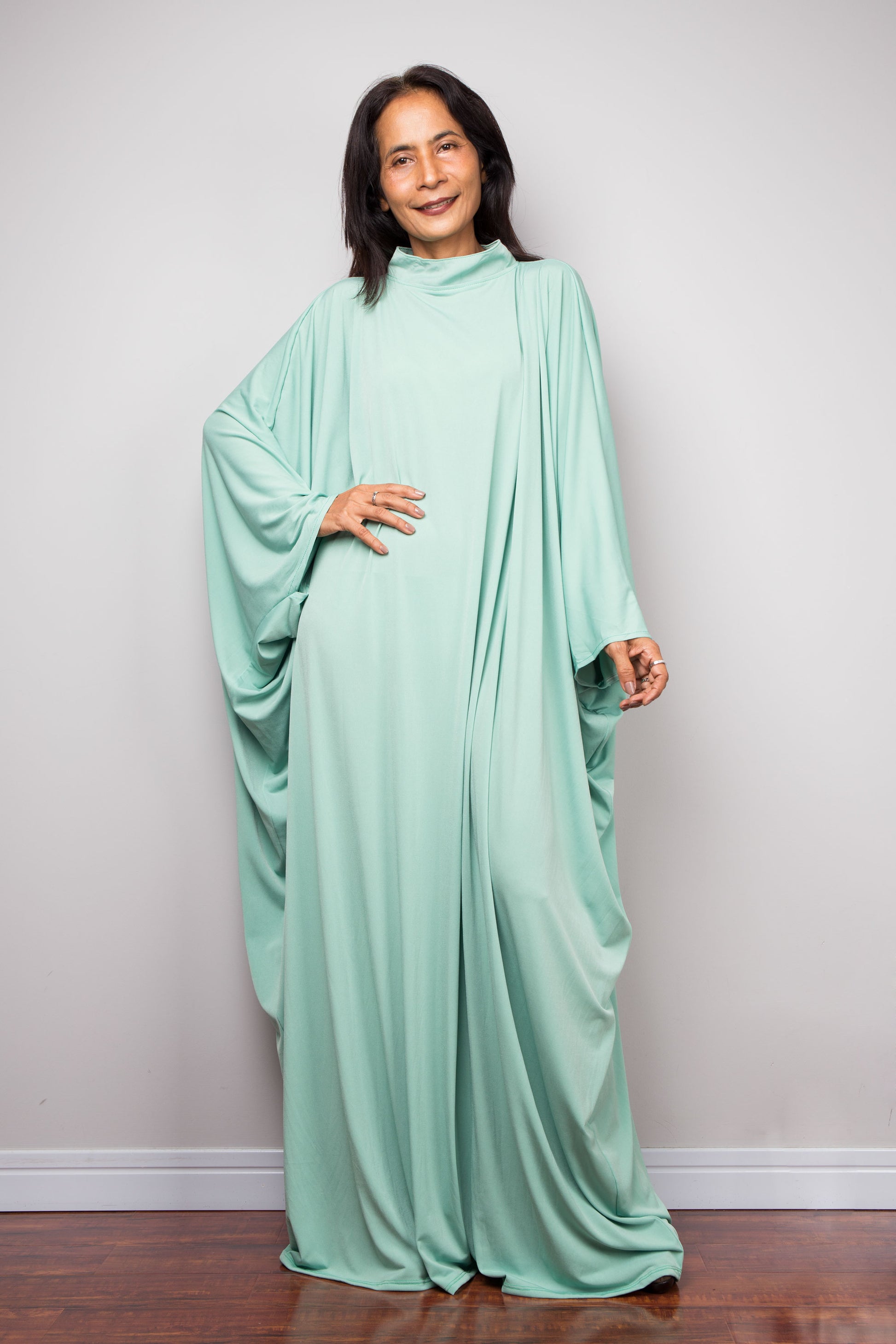 Woman wearing a mint green caftan abaya dress against a plain background