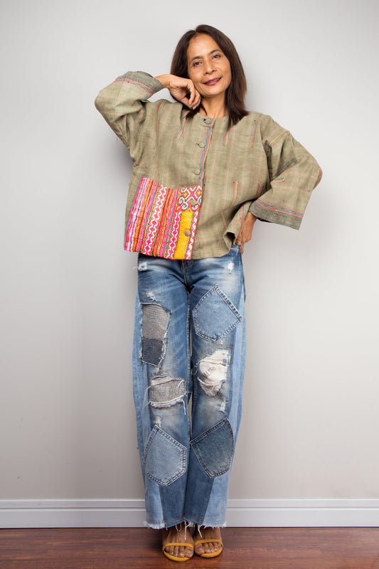 Woman in an olive hemp jacket with patchwork panel by Nuichan, styled with distressed jeans, against a gray wall and wooden floor, accessorized with tan heels.

