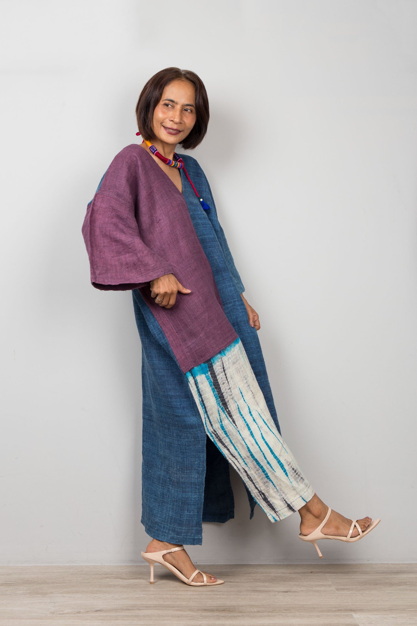 Woman wearing a long purple and blue dress with white and blue striped shibori panel, standing against a plain background.