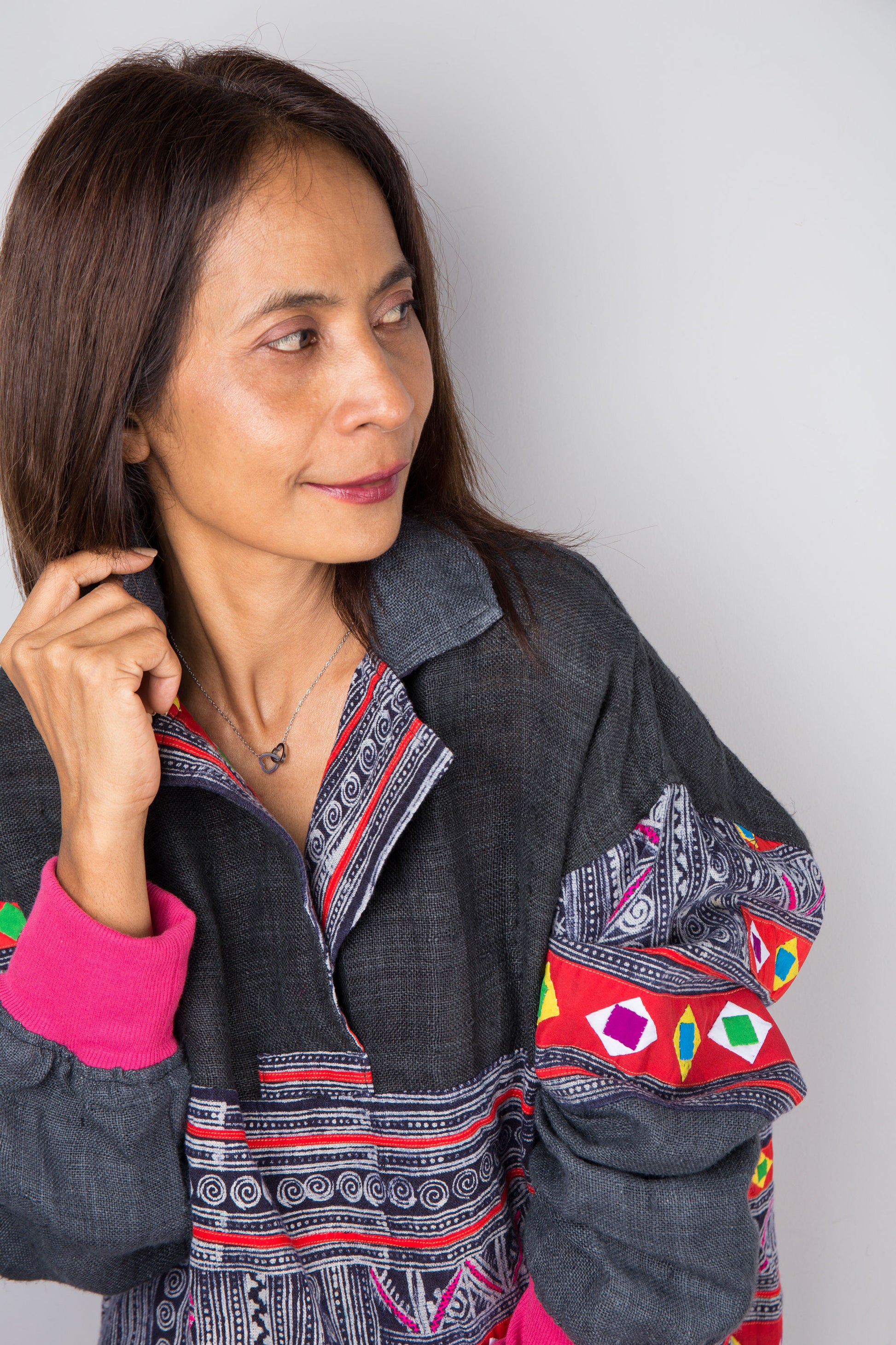 Woman in a hand-batik pullover tunic with patchwork designs by Nuichan, styled with jeans, against a gray wall 