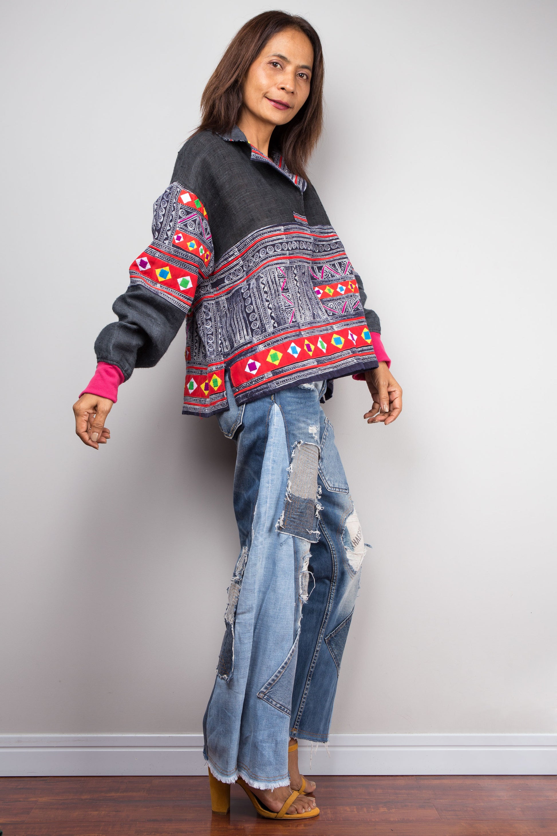Hand-batik pullover tunic with colorful patchwork accents by Nuichan on a woman, paired with distressed jeans, set against a gray wall and wooden floor, with a necklace.

