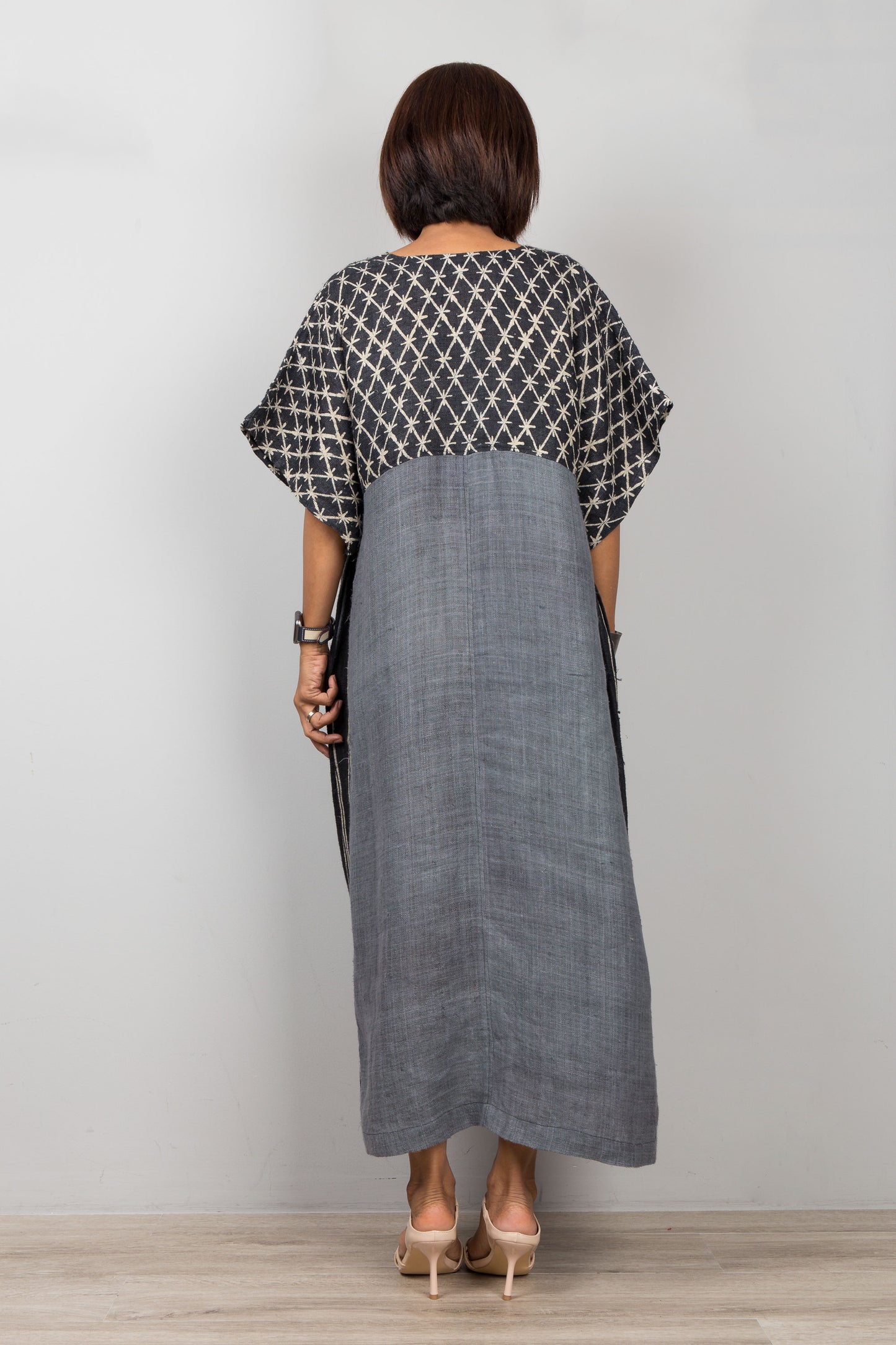 Woman wearing a black and white patterned top with a long gray dress against a plain background