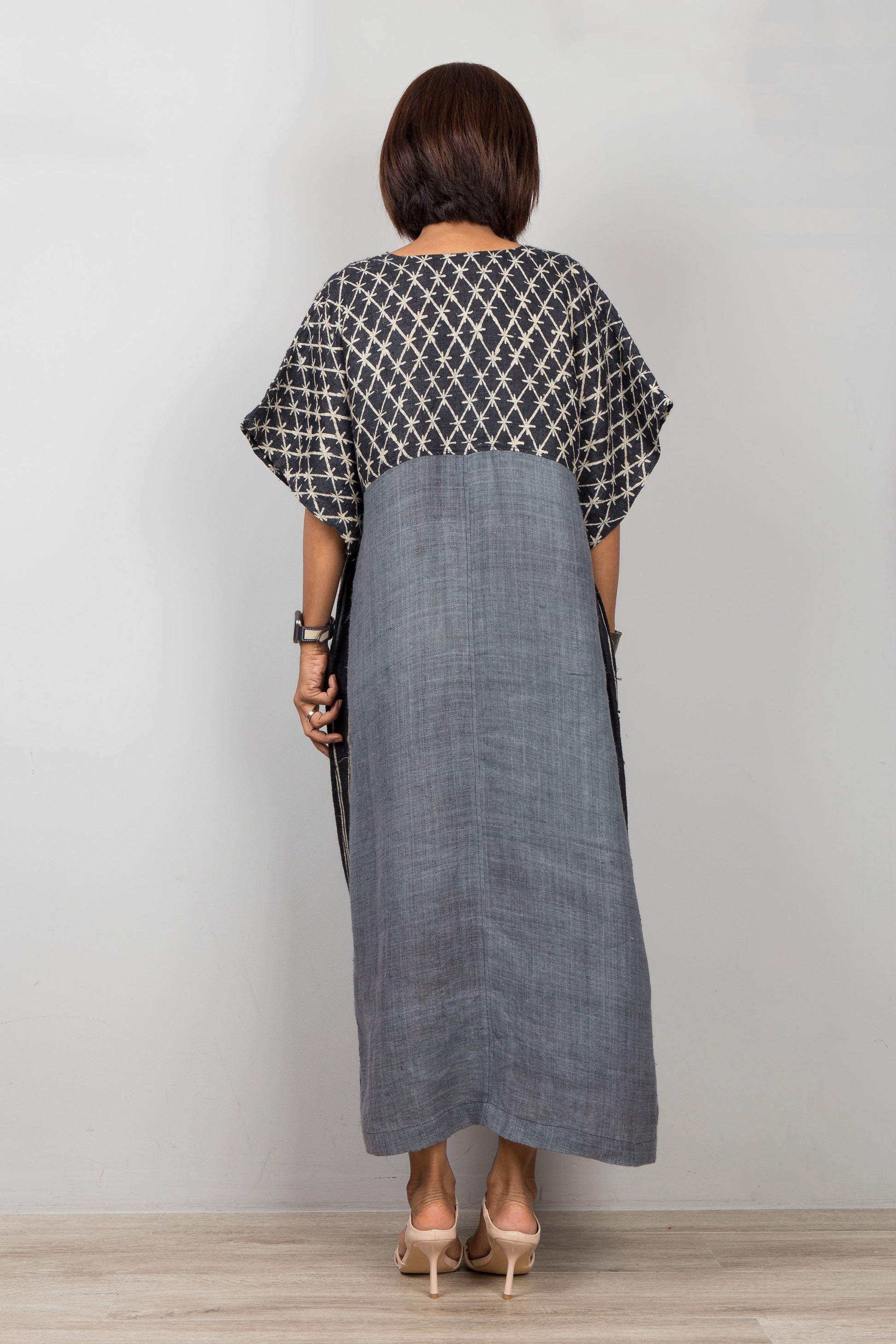 Woman wearing a black and white patterned top with a long gray dress against a plain background