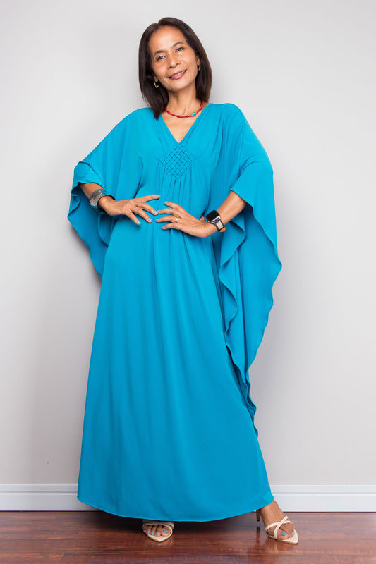 Petite Woman wearing a blue kaftan dress standing against a white wall.