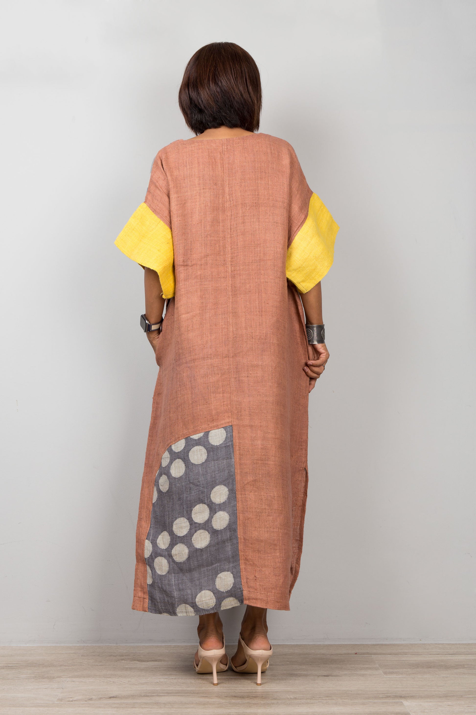 Woman wearing a long, patterned brown hemp petite kaftan dress with yellow sleeves against a plain background