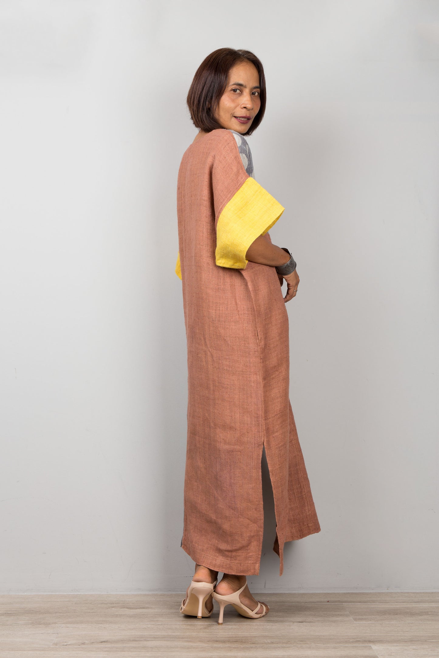 Woman wearing a long brown dress with yellow sleeves against a plain background