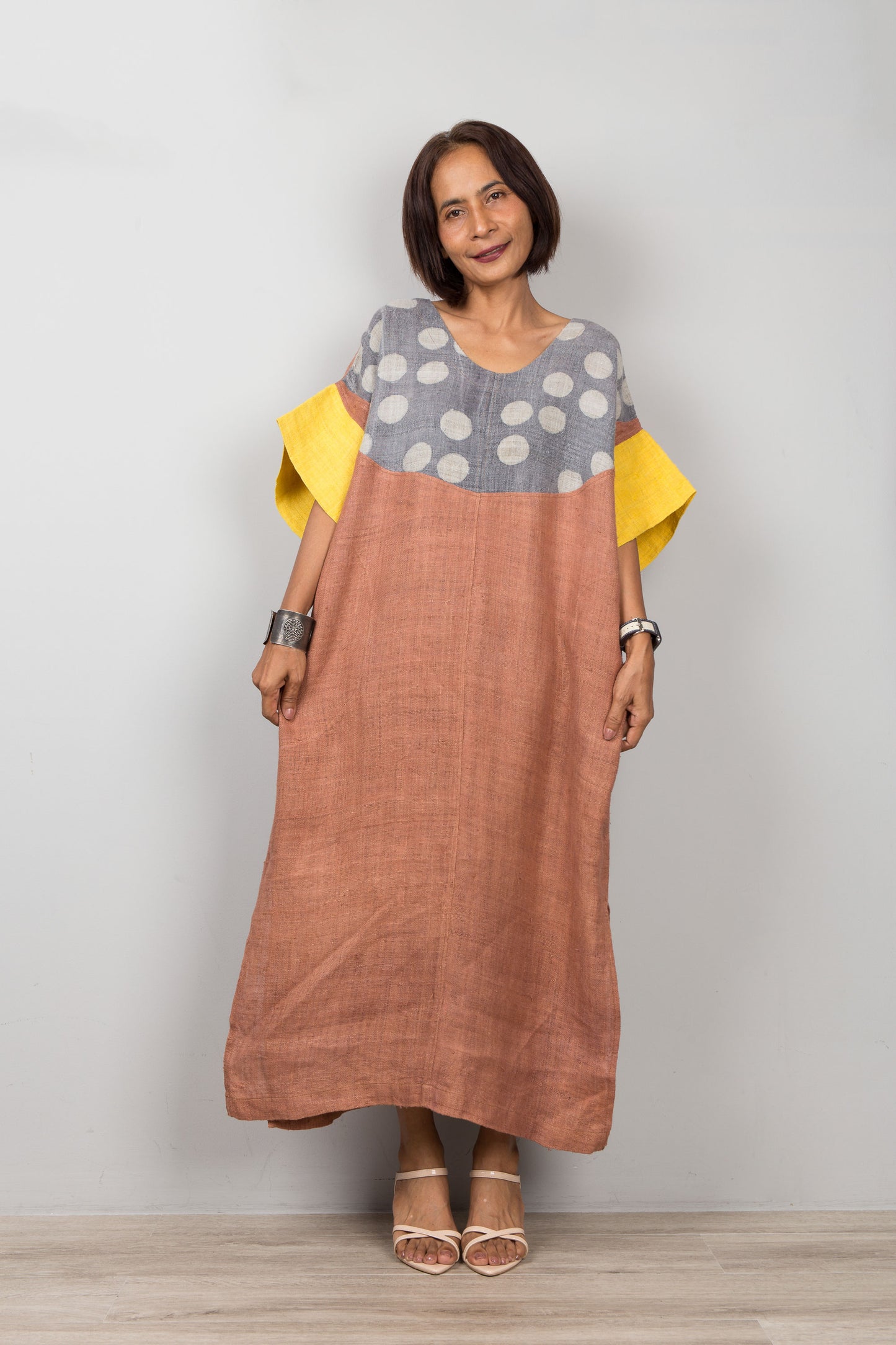 Woman wearing a long, two-tone petite kaftan dress with a polka dot pattern on a plain background