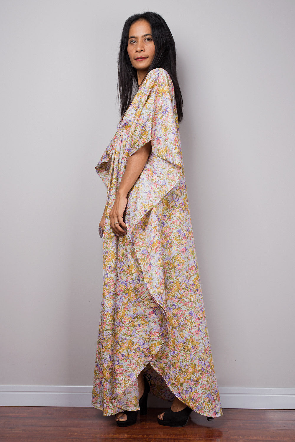 Petite woman wearing a floral caftan dress against a plain background