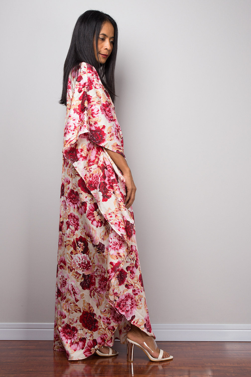Woman wearing a petite floral caftan dress against a plain background